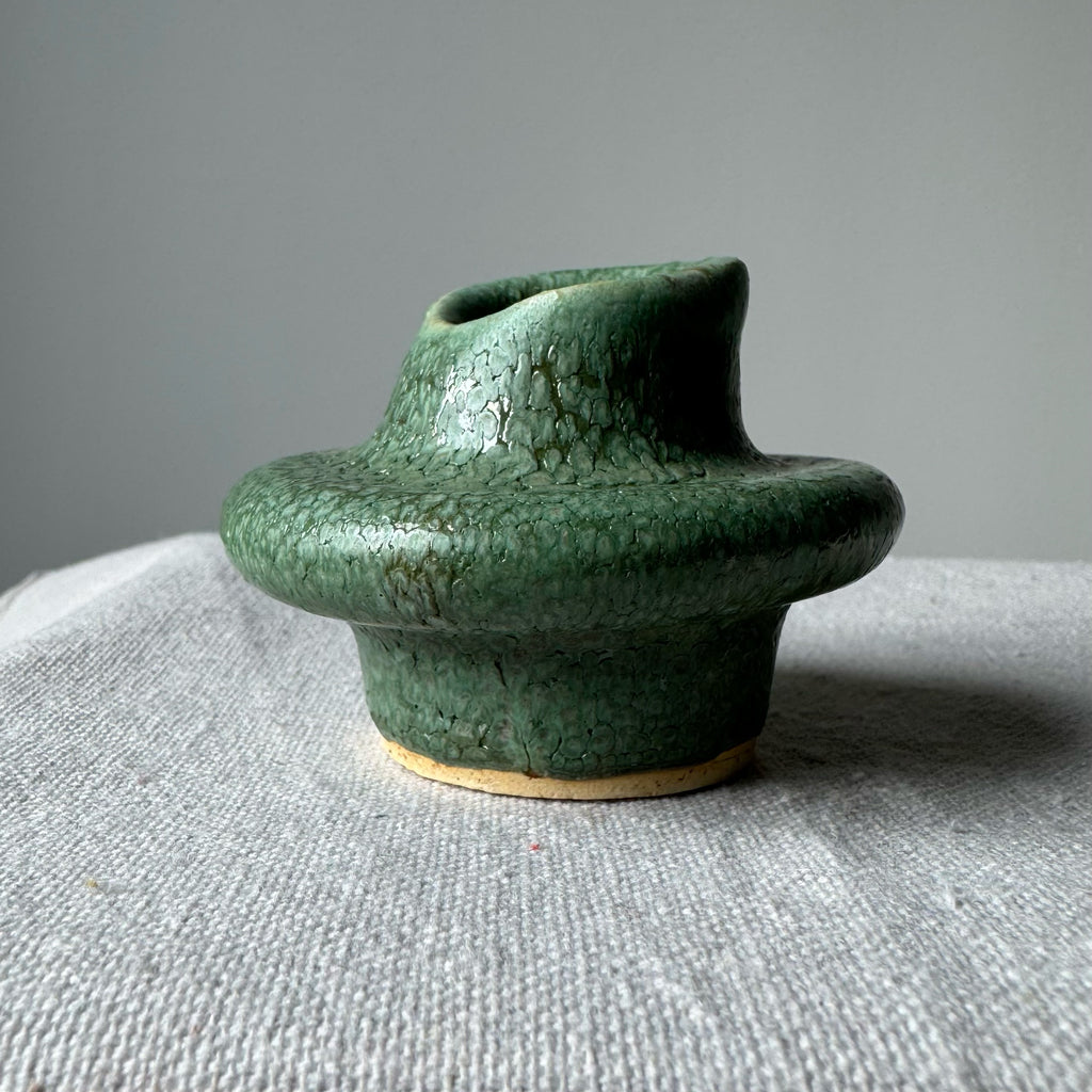Green ceramic vase on a textured surface with a gray background