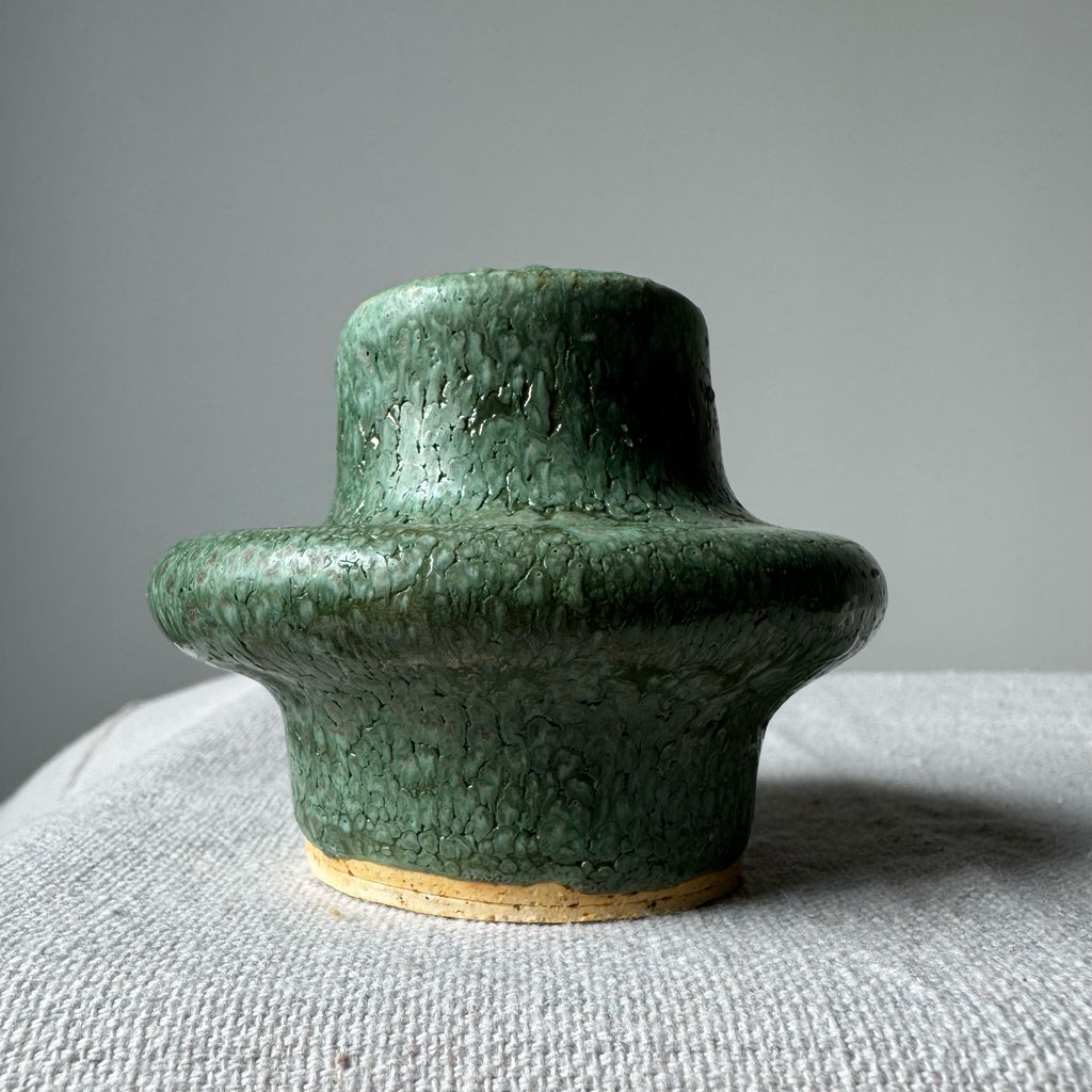 Green ceramic vase on a textured surface with a gray background