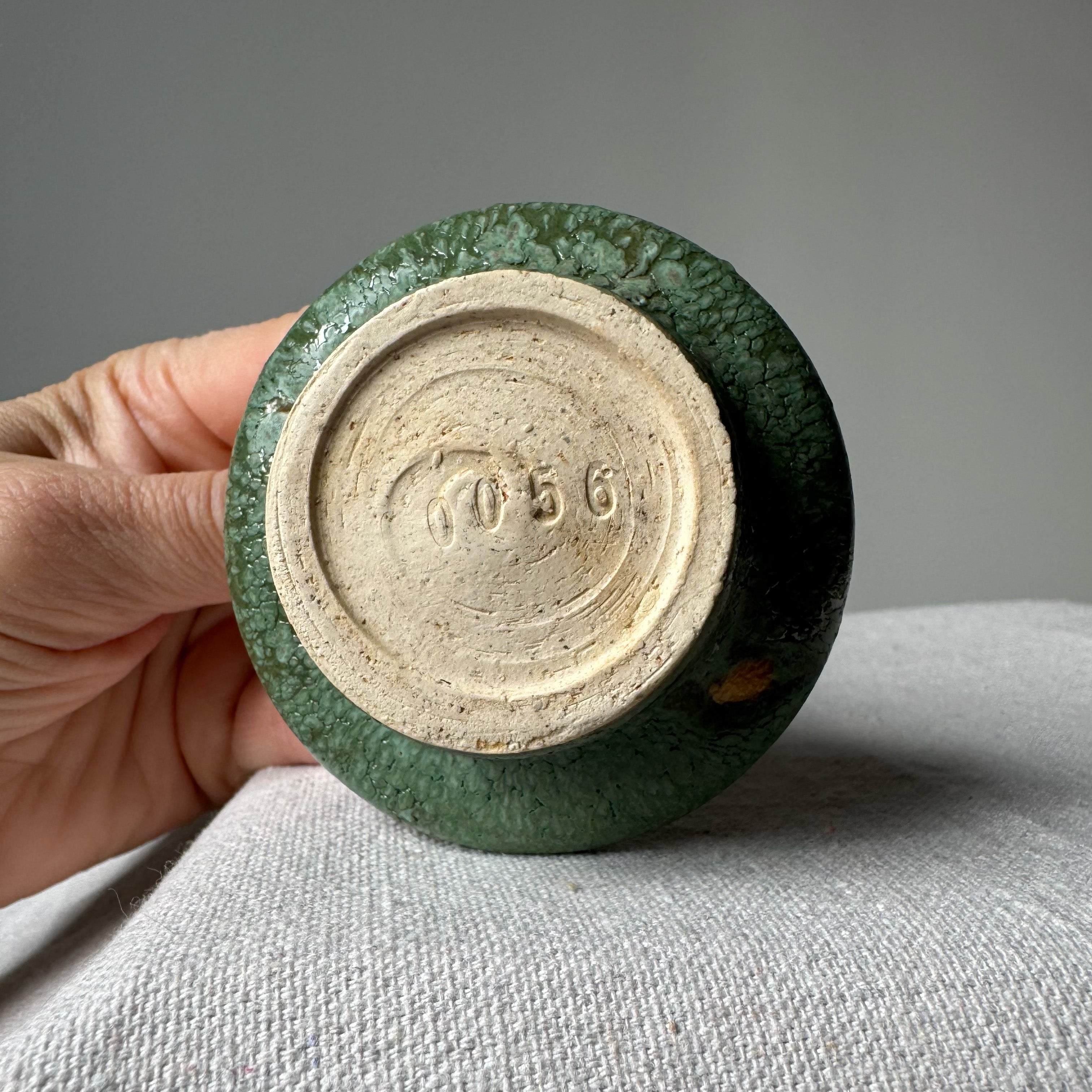 Green ceramic object with a beige circular mark held by a hand on a gray surface.