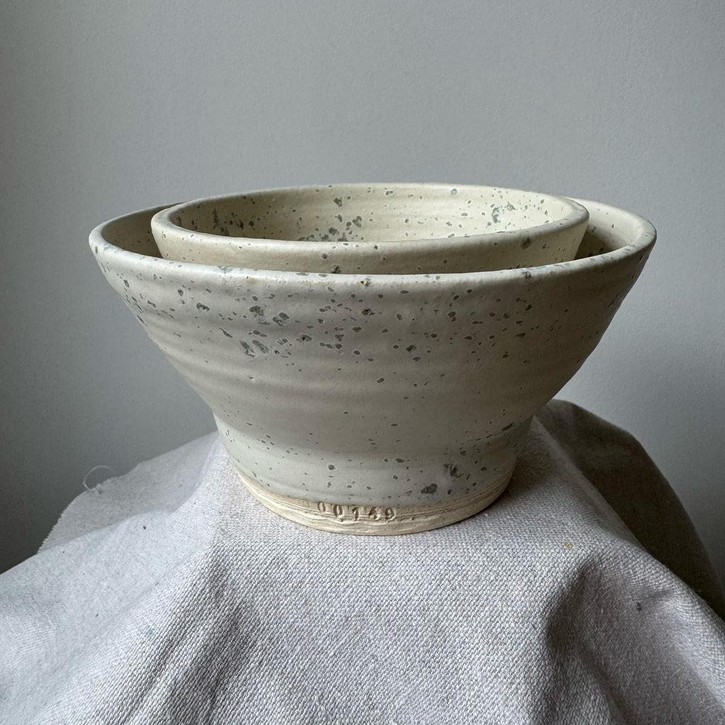 Two ceramic bowls stacked on a textured surface with a neutral background