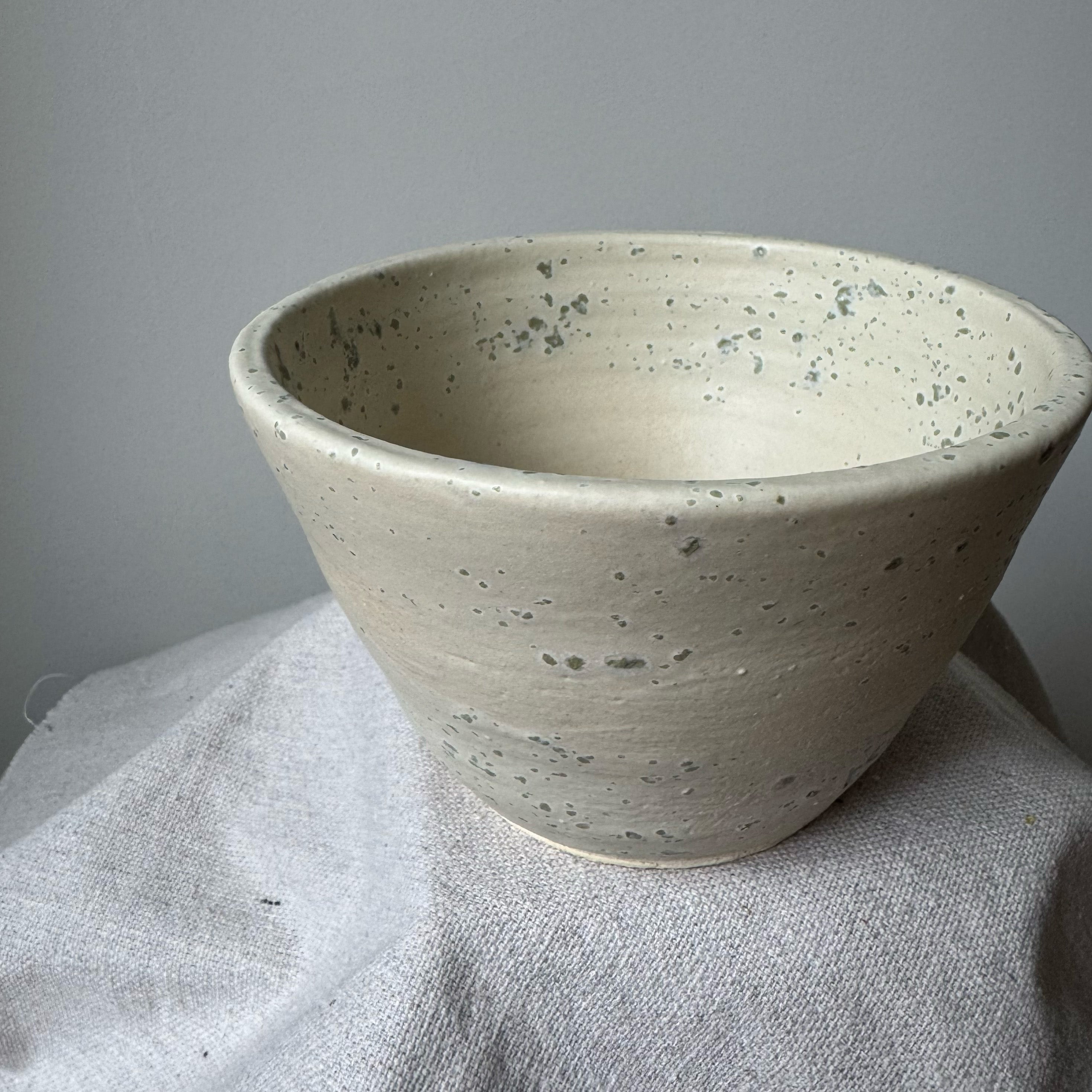 Speckled beige ceramic bowl on a gray surface with a neutral background