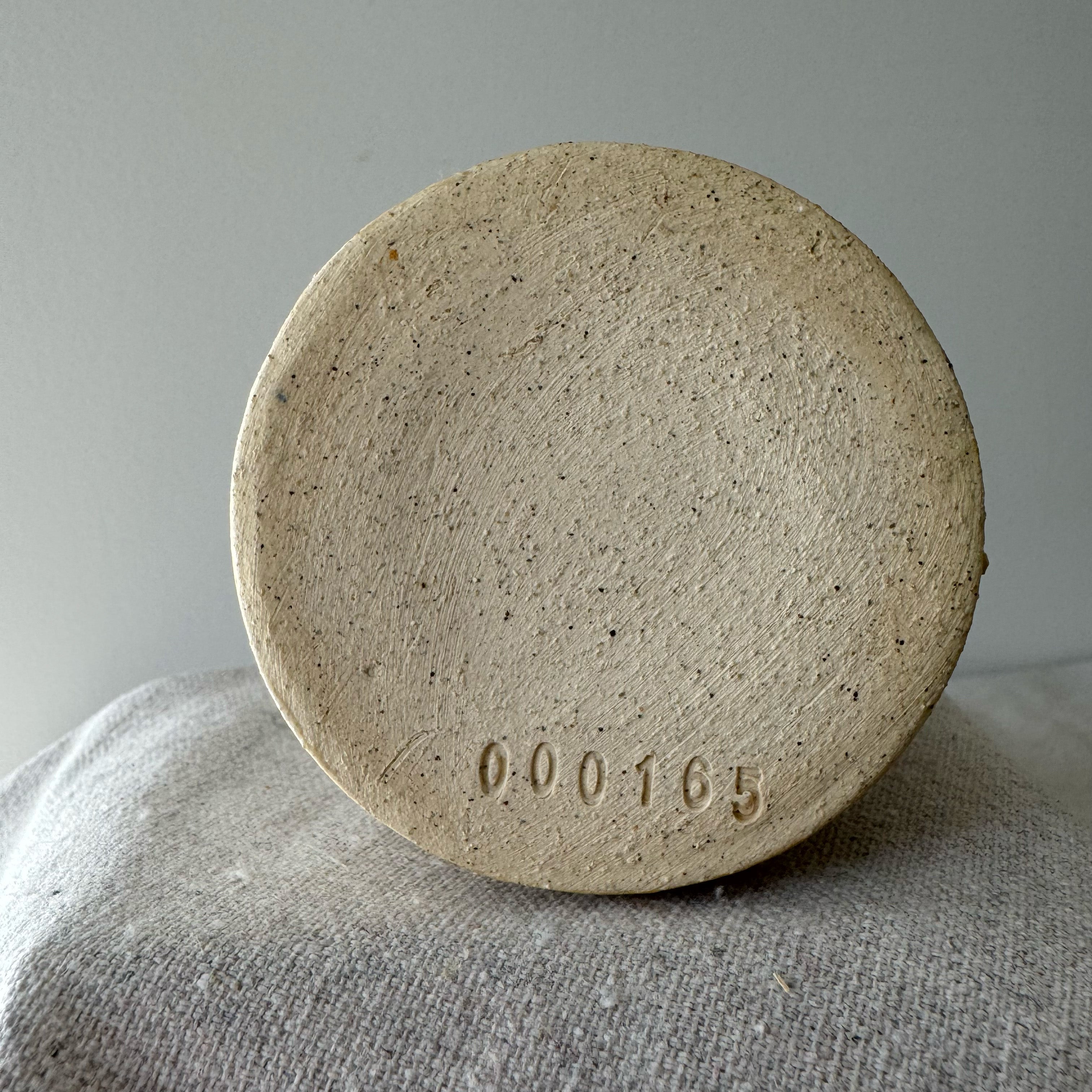 Round stone object with '000165' embossed on it, placed on a textured surface.