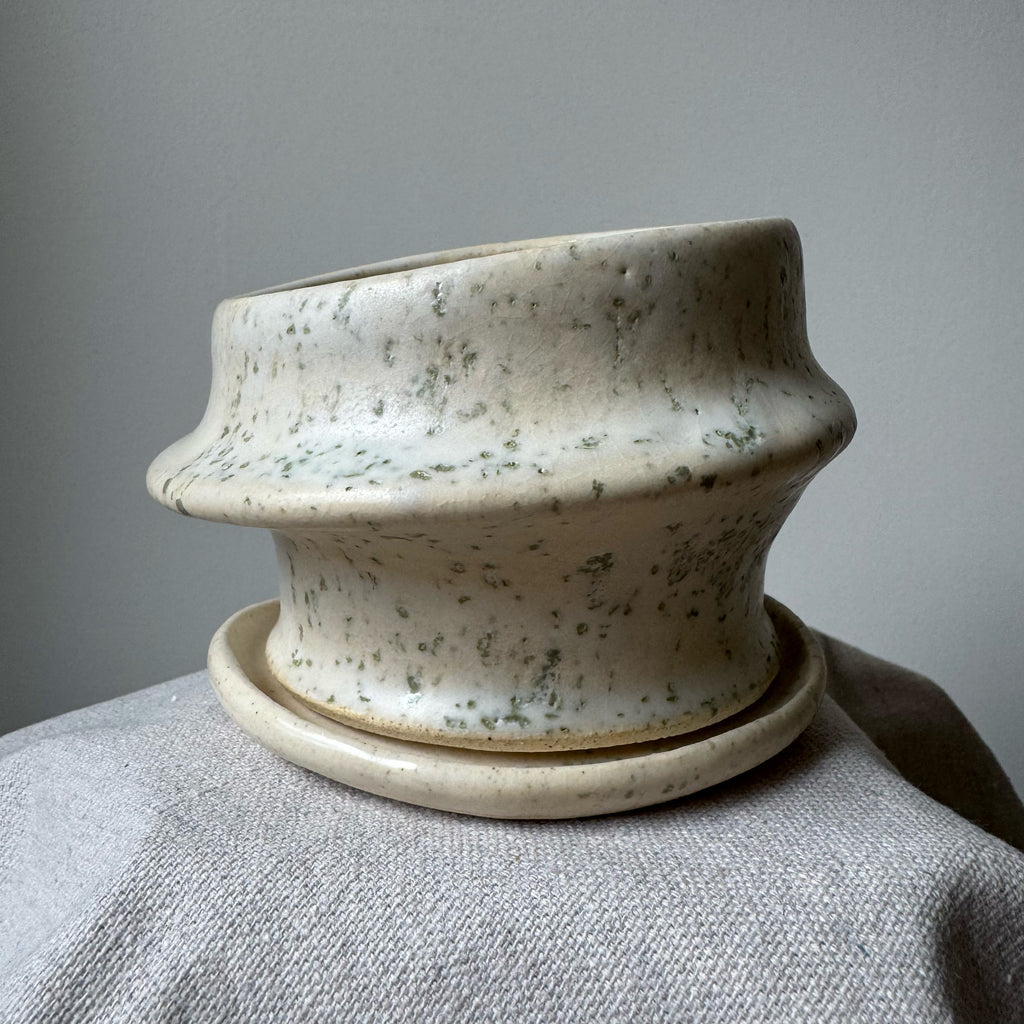 Speckled ceramic pot on a gray surface with a neutral background