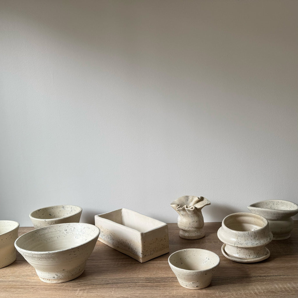 Collection of ceramic bowls and containers on a wooden surface with a plain background