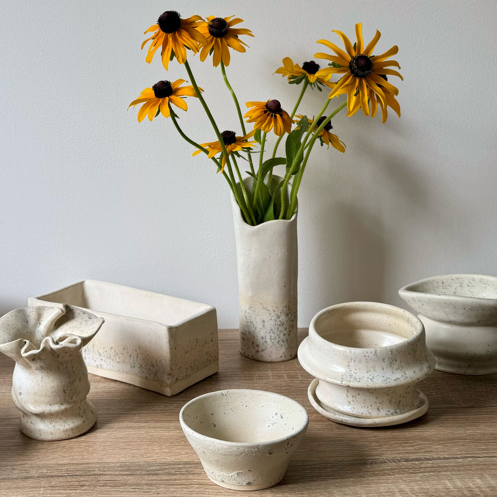 Collection of ceramic pots and a vase with yellow flowers on a wooden surface.