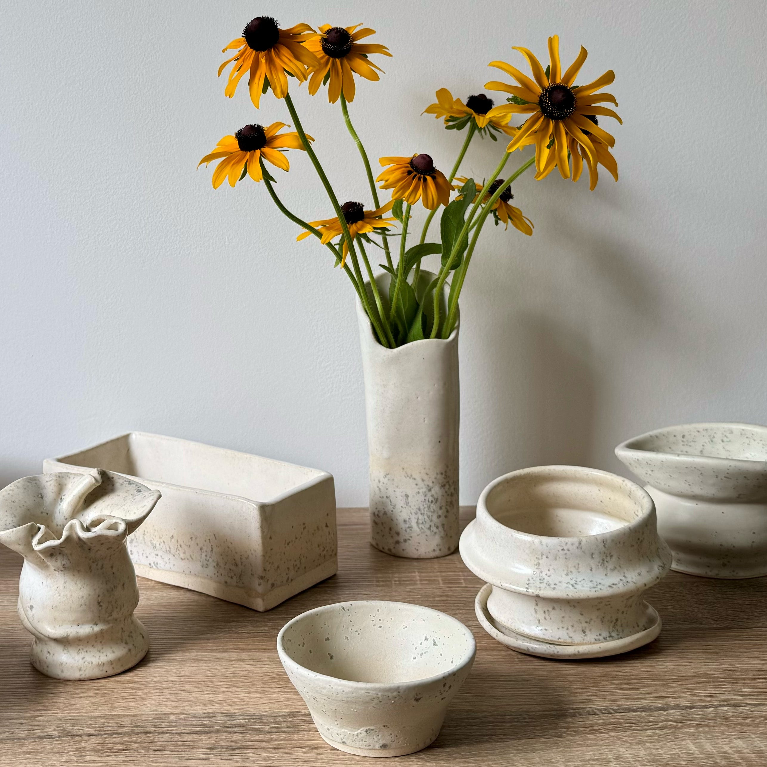 Collection of ceramic pots and a vase with yellow flowers on a wooden surface.