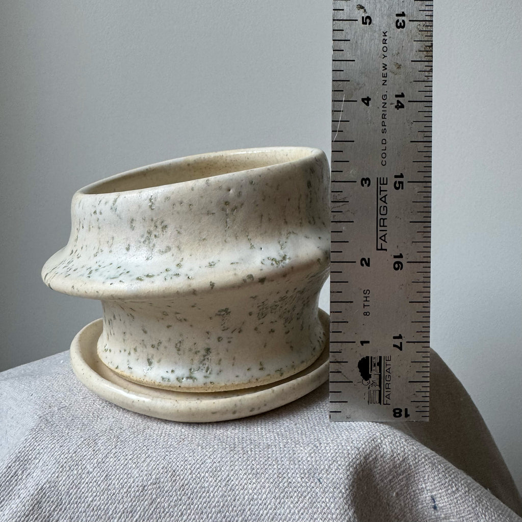 Speckled ceramic planter with saucer next to a ruler for scale on a gray surface.
