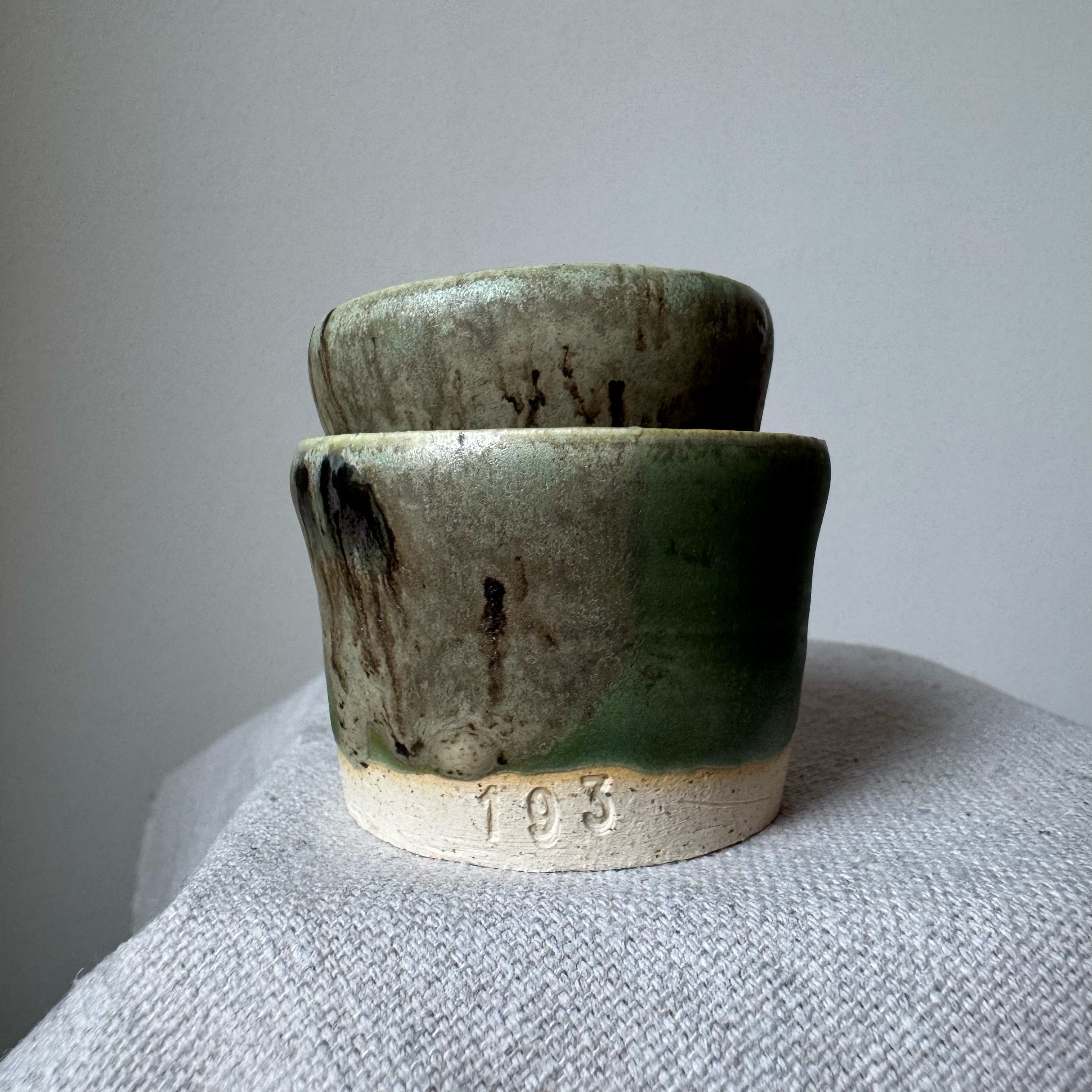 Two green ceramic pots stacked on a textured surface with a neutral background