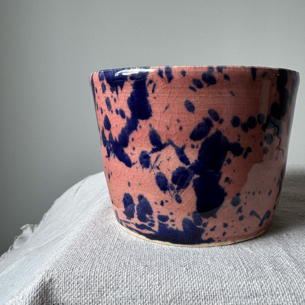Ceramic cup with pink and blue splatter design on a gray surface