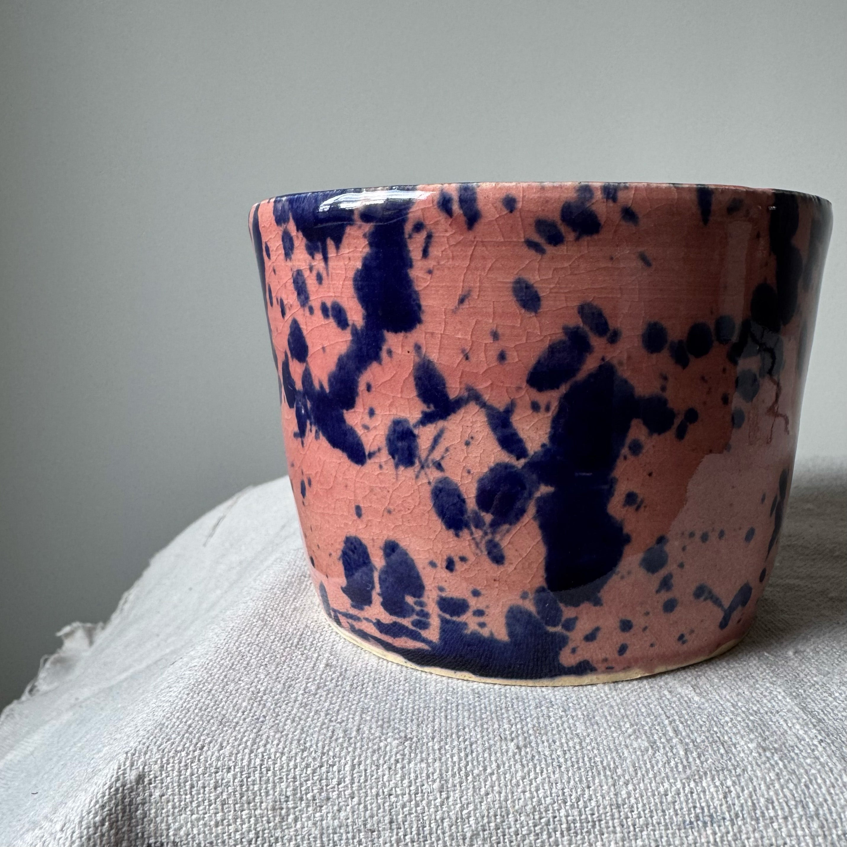 Ceramic cup with pink and blue splatter design on a gray surface