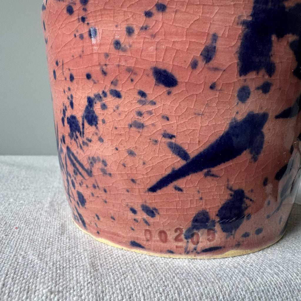Ceramic vase with pink glaze and blue speckles on a textured surface