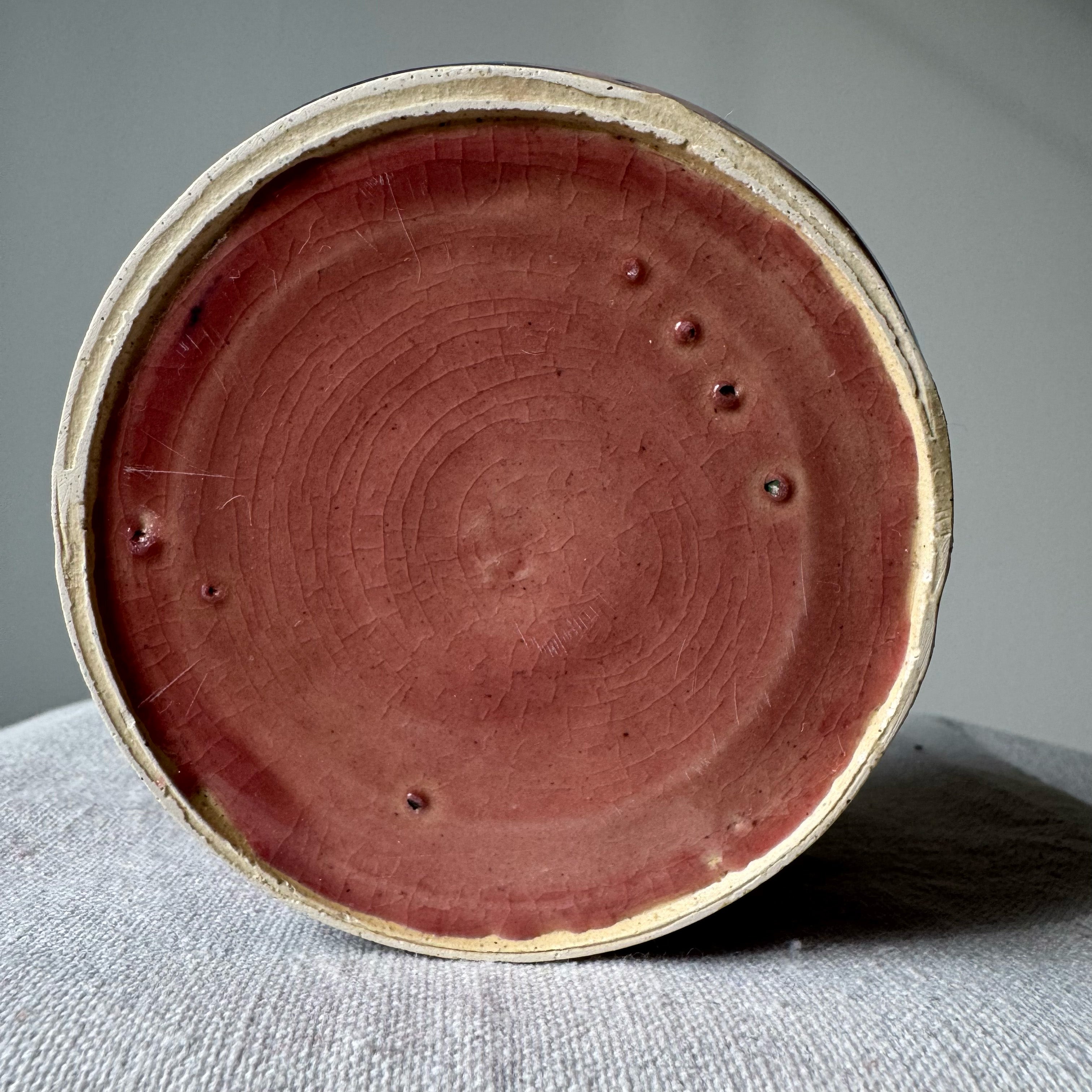 Close-up of a ceramic pot with a reddish-brown interior on a gray surface.