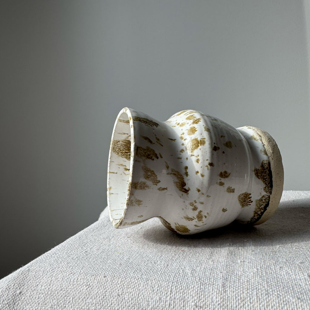 Ceramic vase with brown speckles on a gray surface against a gray background