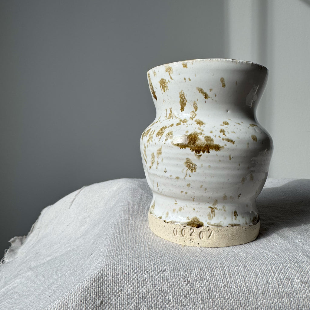 White ceramic vase with brown speckles on a textured surface