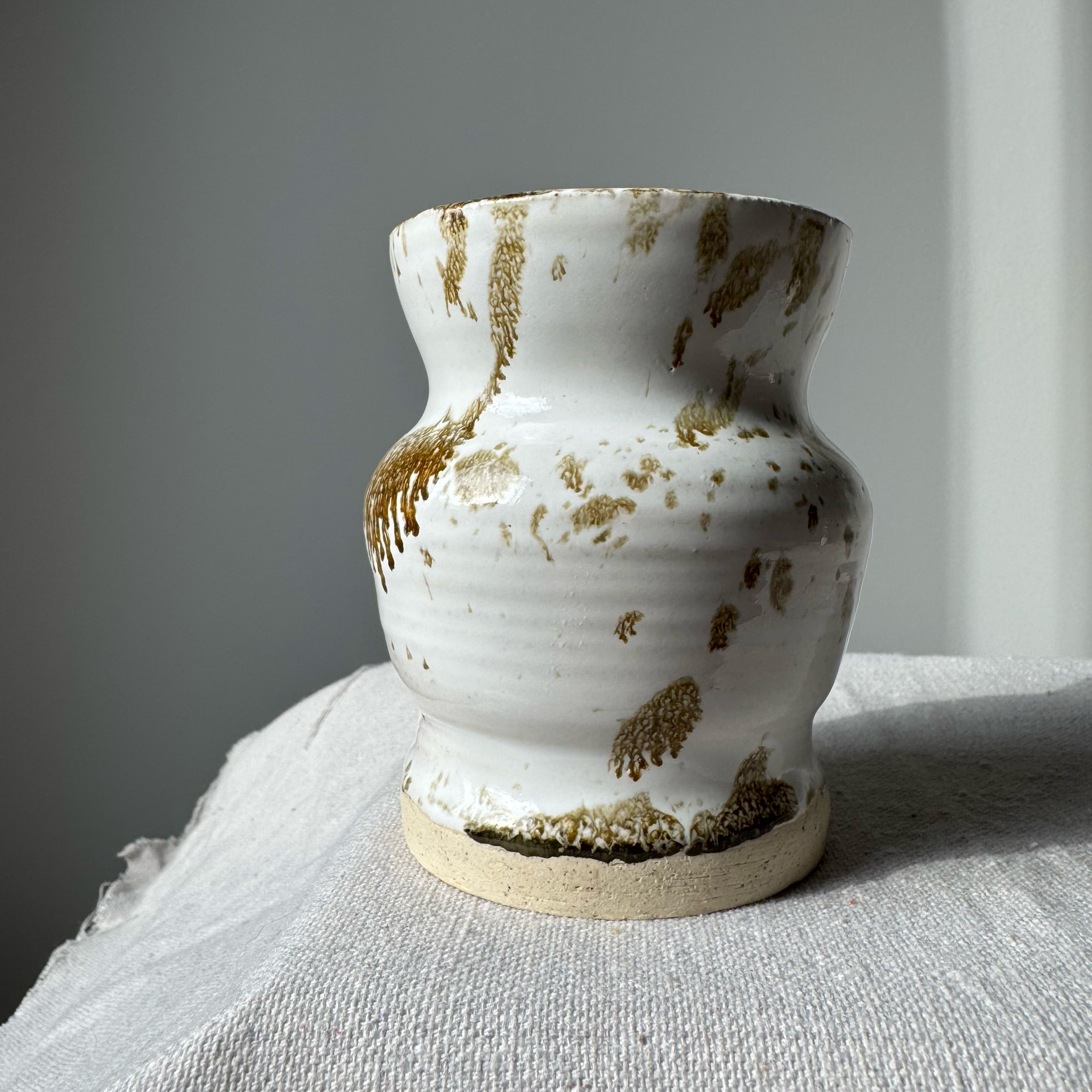 White ceramic vase with brown speckles on a gray surface