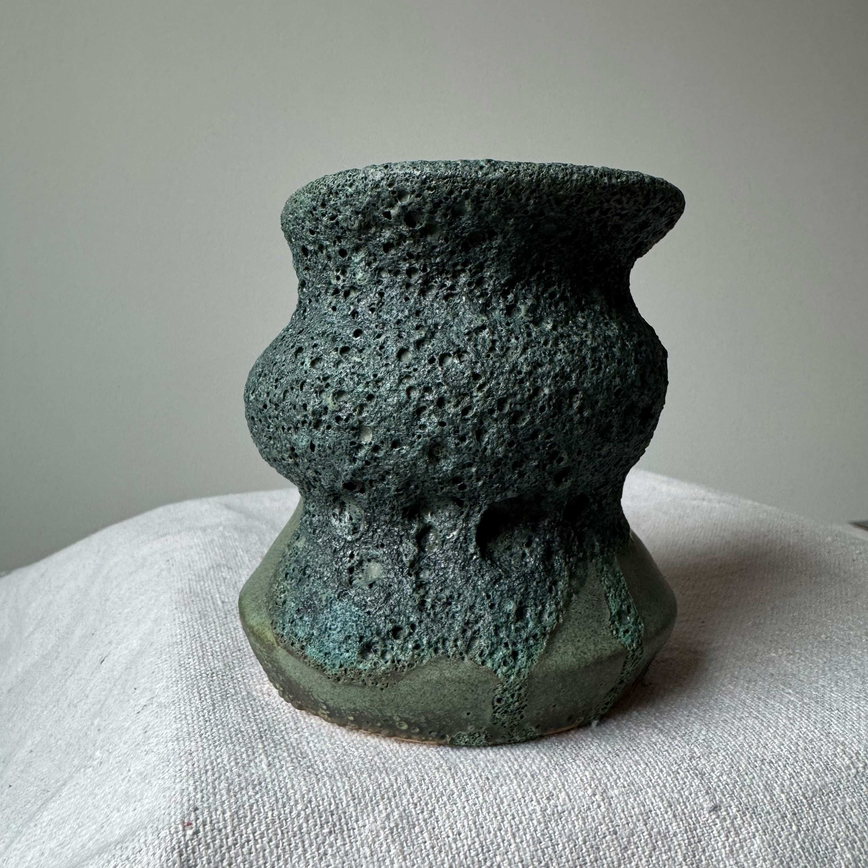 Textured green ceramic vase on a light fabric surface with a neutral background