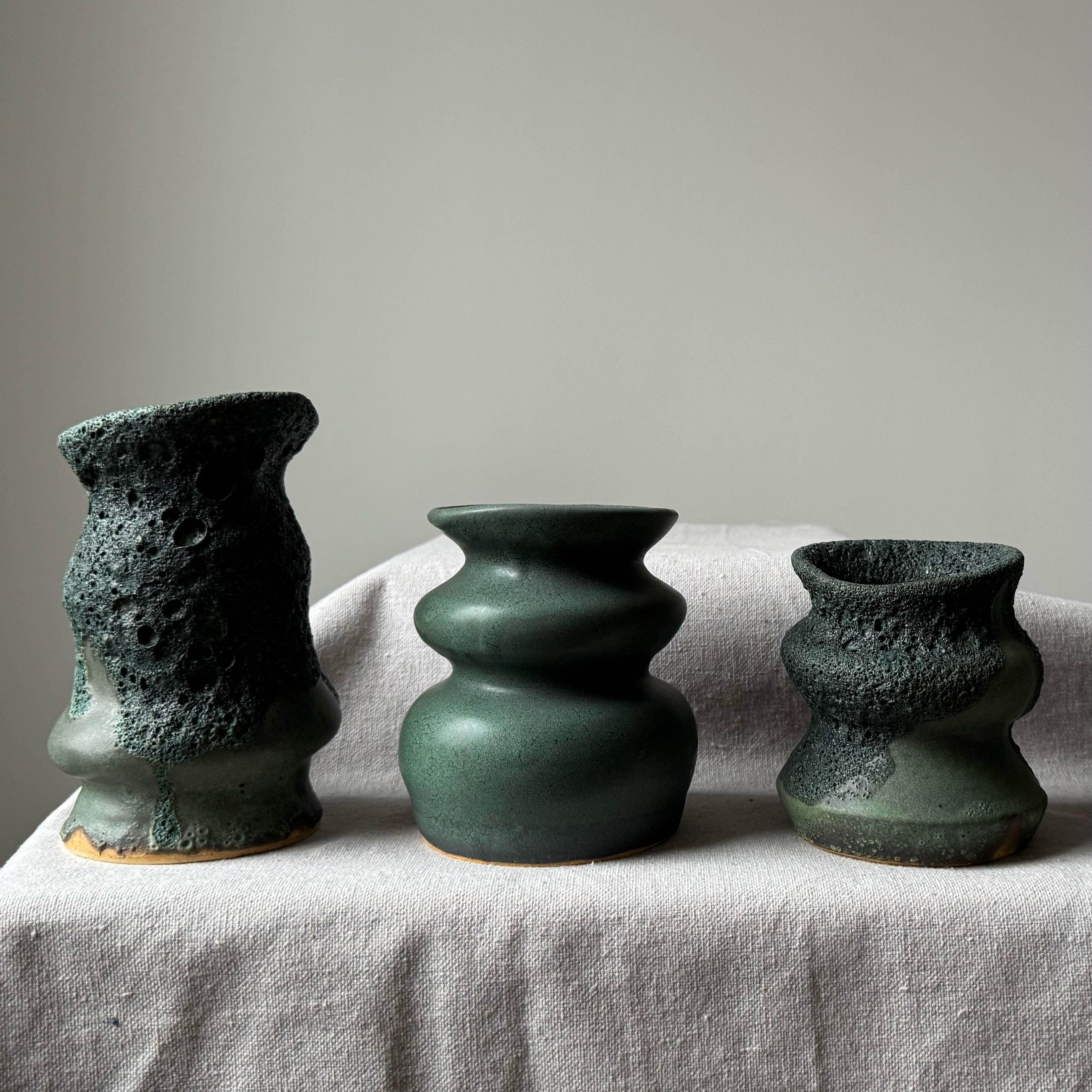 Three green ceramic vases of different shapes on a light fabric surface with a neutral background