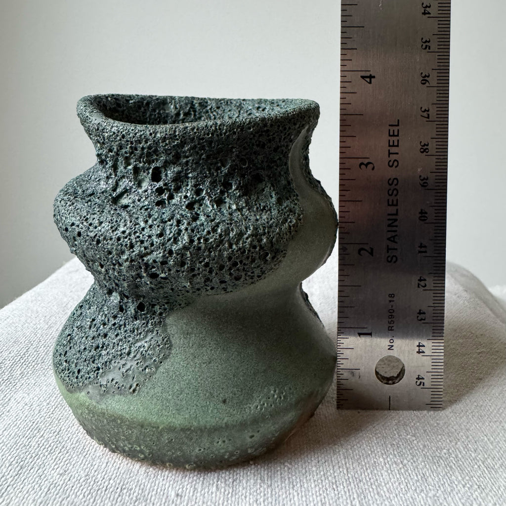Green ceramic vase with textured surface next to a ruler on a light background