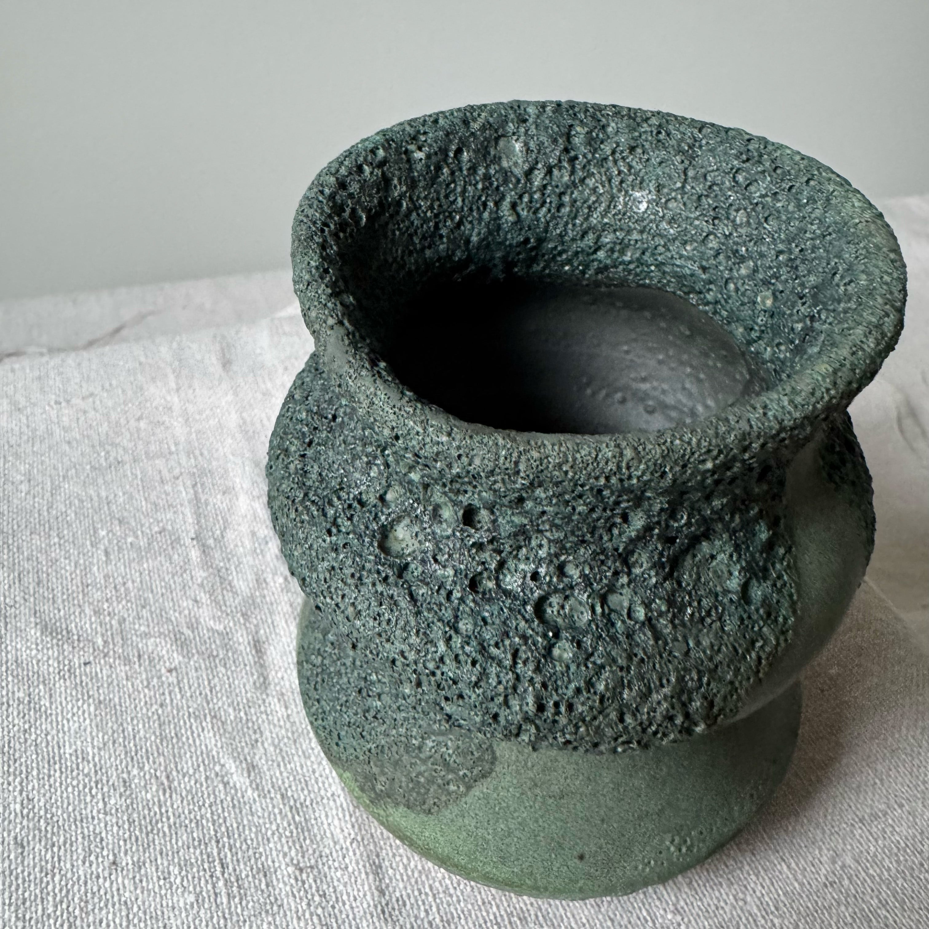 Textured green ceramic pot on a light fabric background