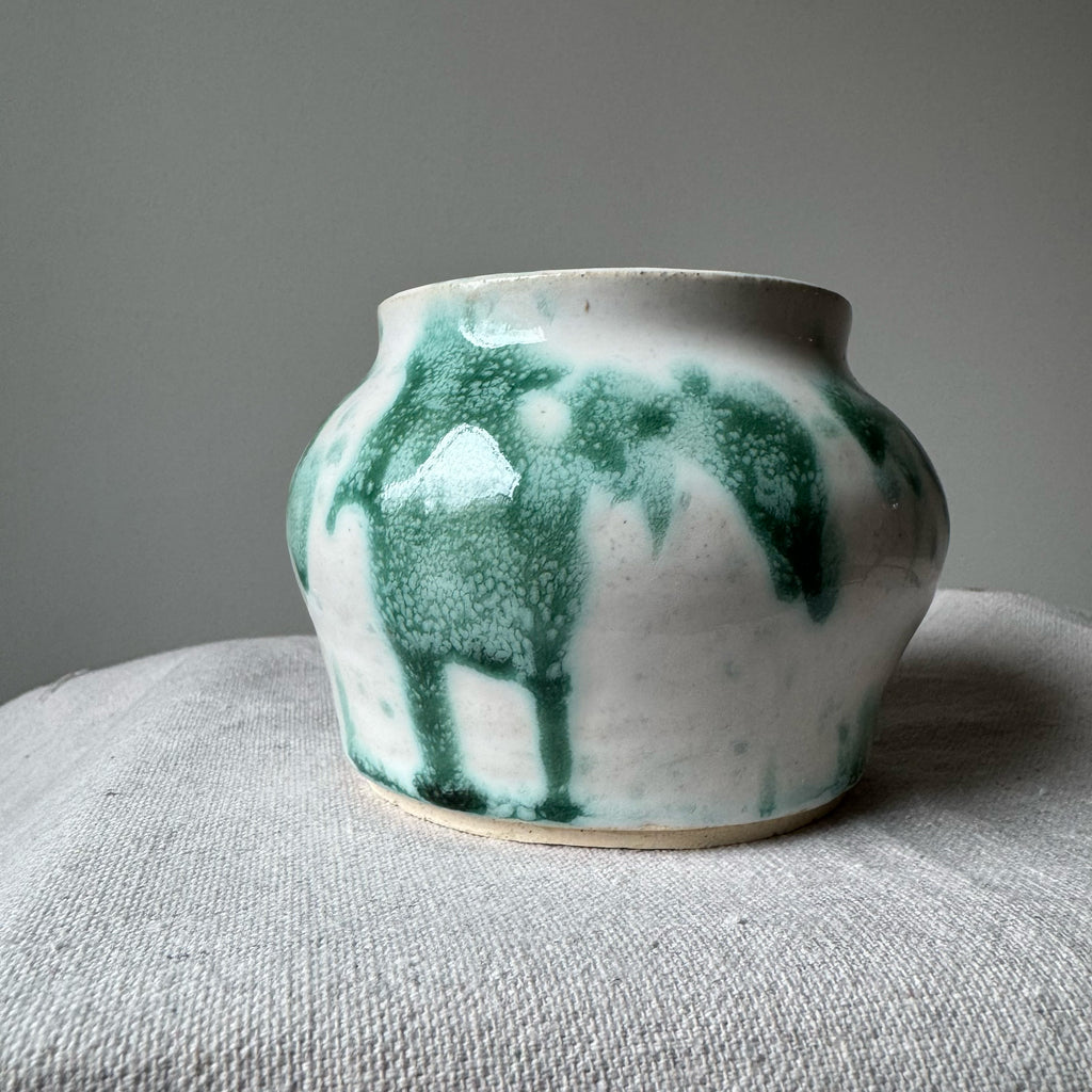 Ceramic pot with green and white glaze on a gray surface