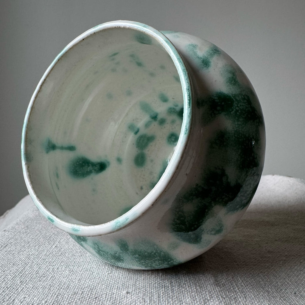 Ceramic bowl with green speckled pattern on a gray surface