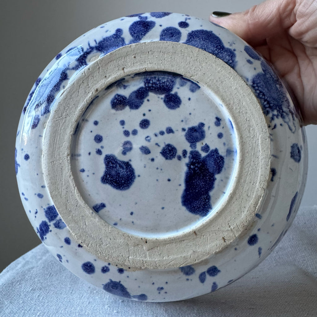 Ceramic pot with blue speckled design held by a hand against a neutral background