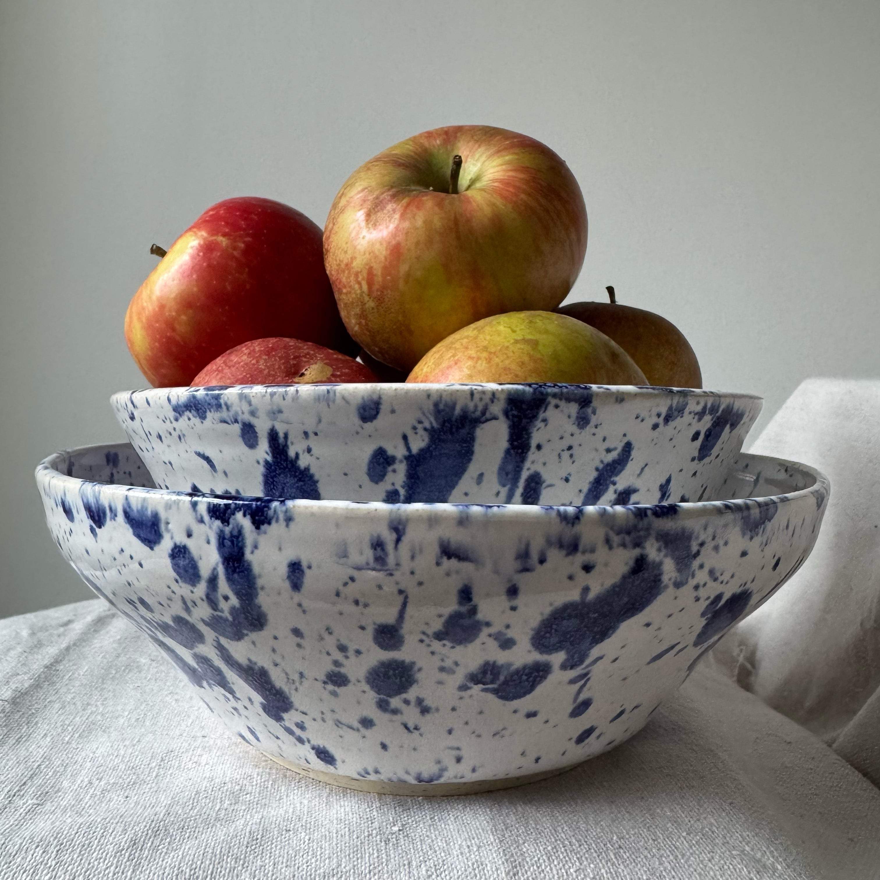 Blue and white speckled bowls with apples on a light surface