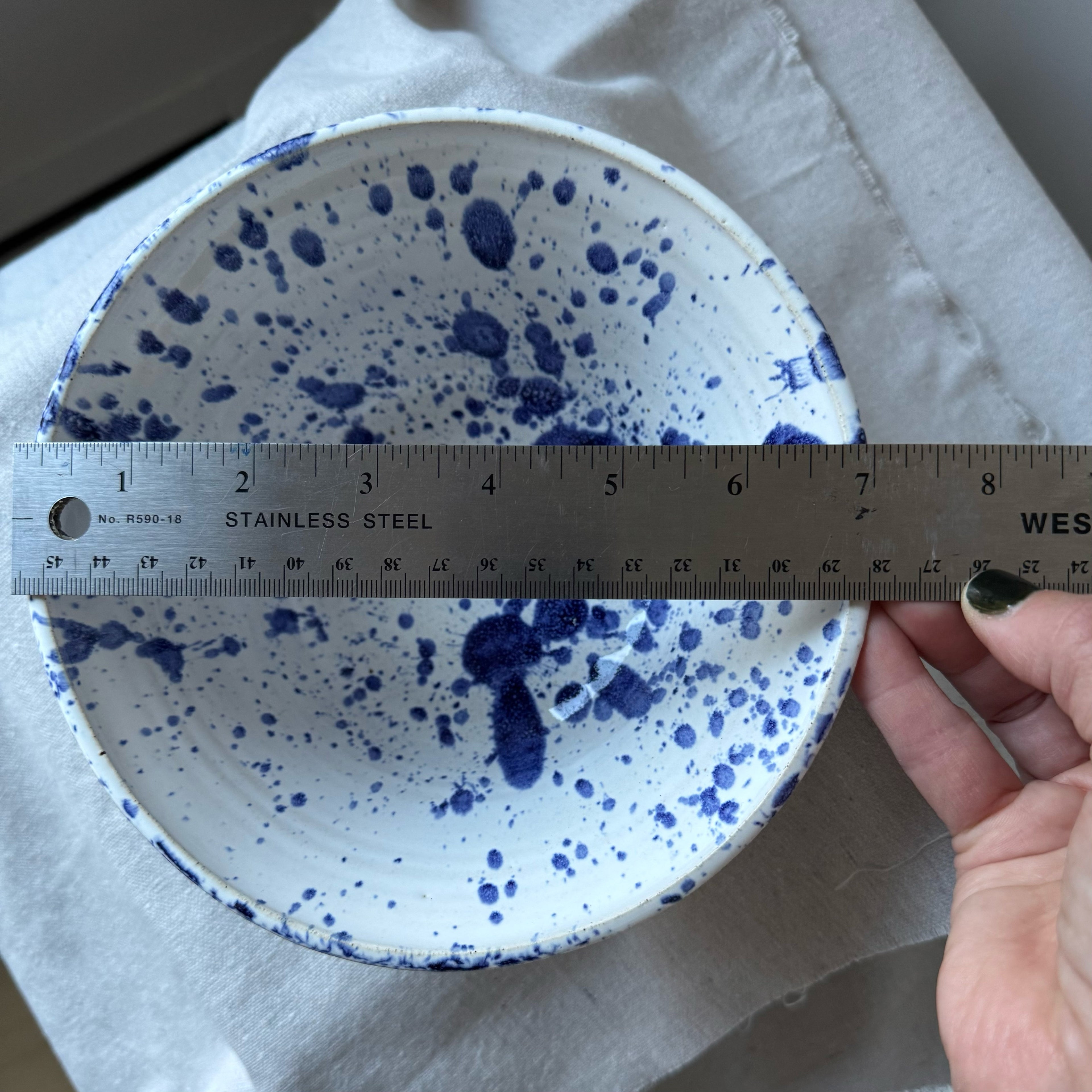 White ceramic bowl with blue speckles being measured with a ruler