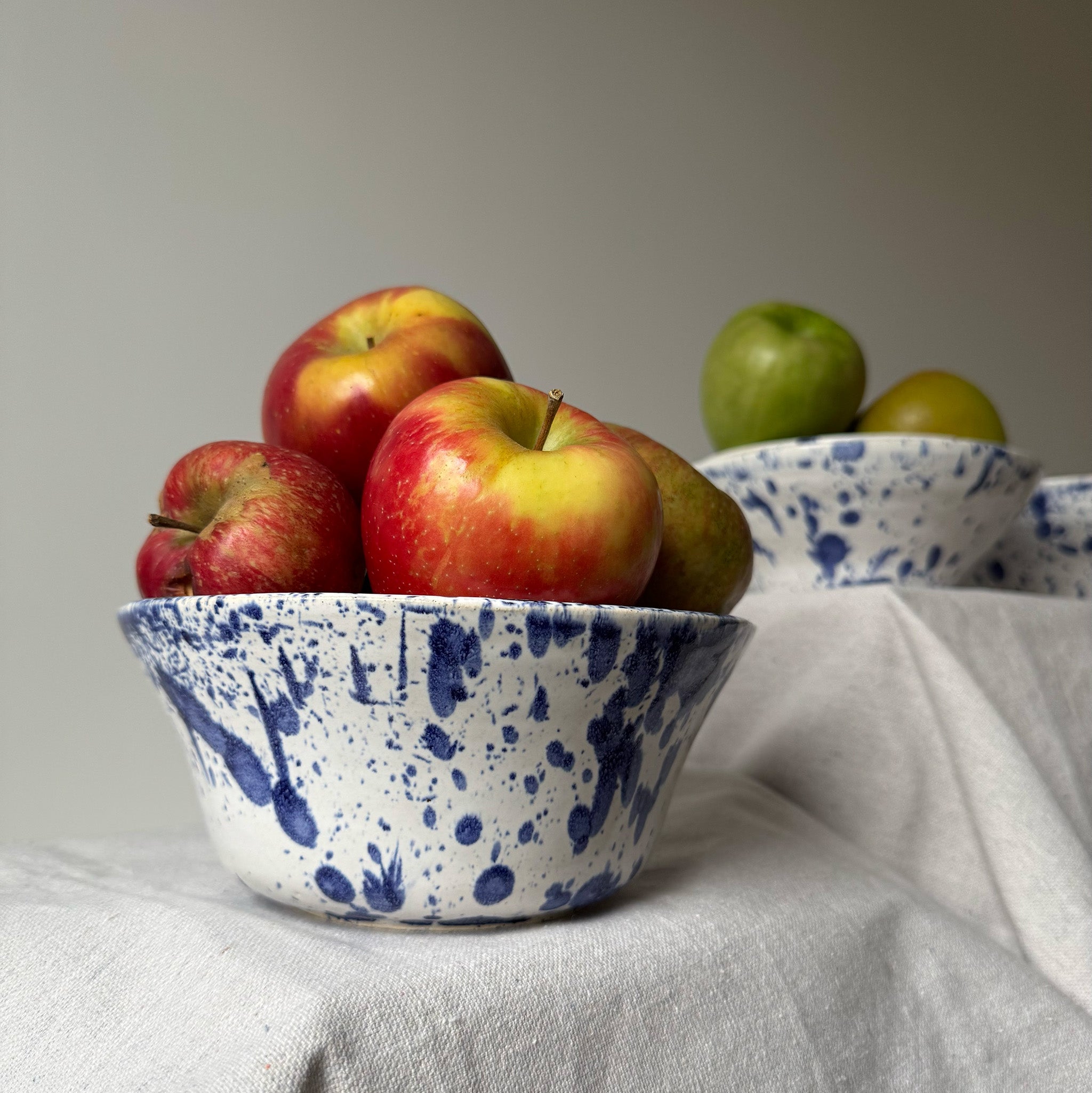 Blue and white speckled bowl with apples on a light gray surface