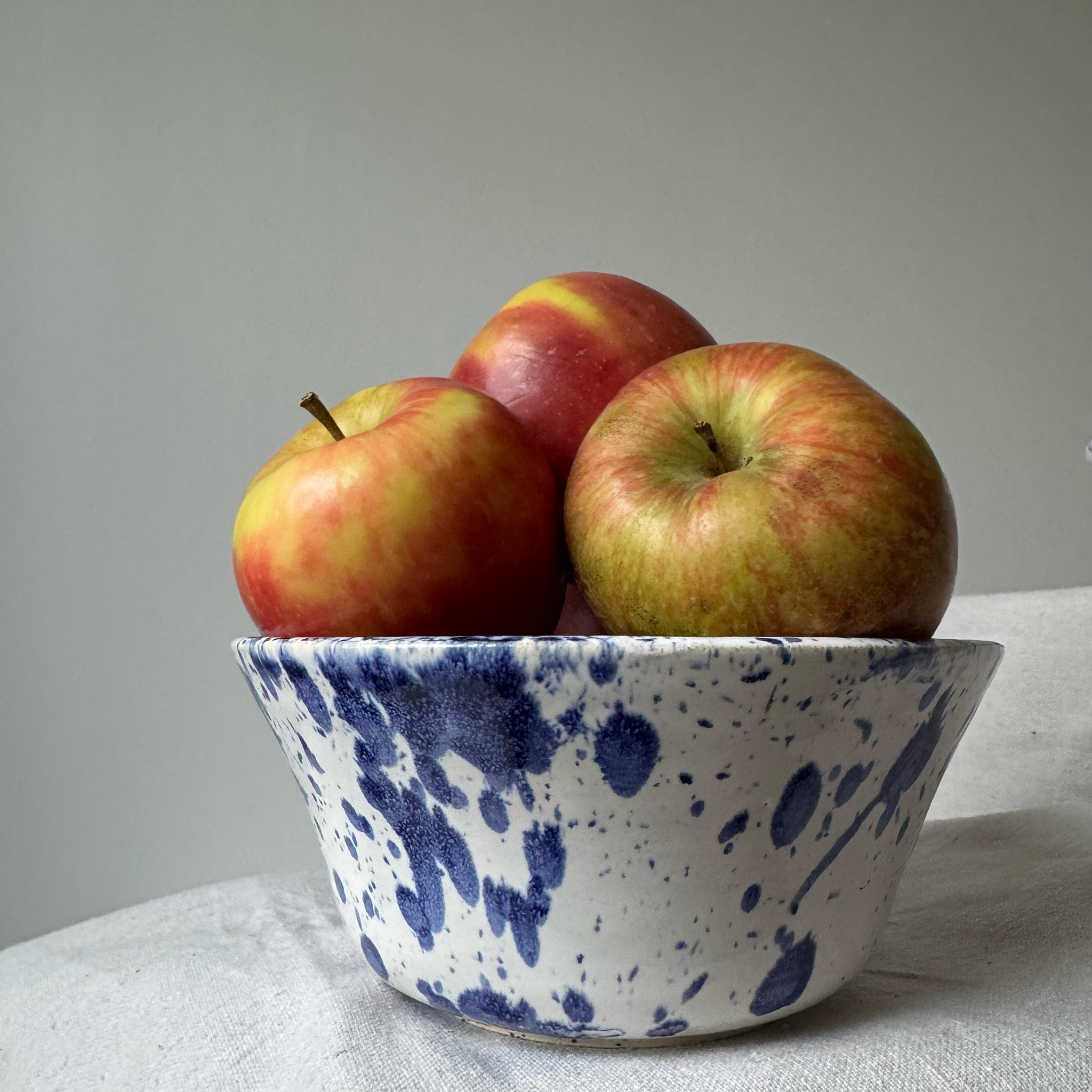 Blue and white speckled ceramic bowl with apples on a light gray background