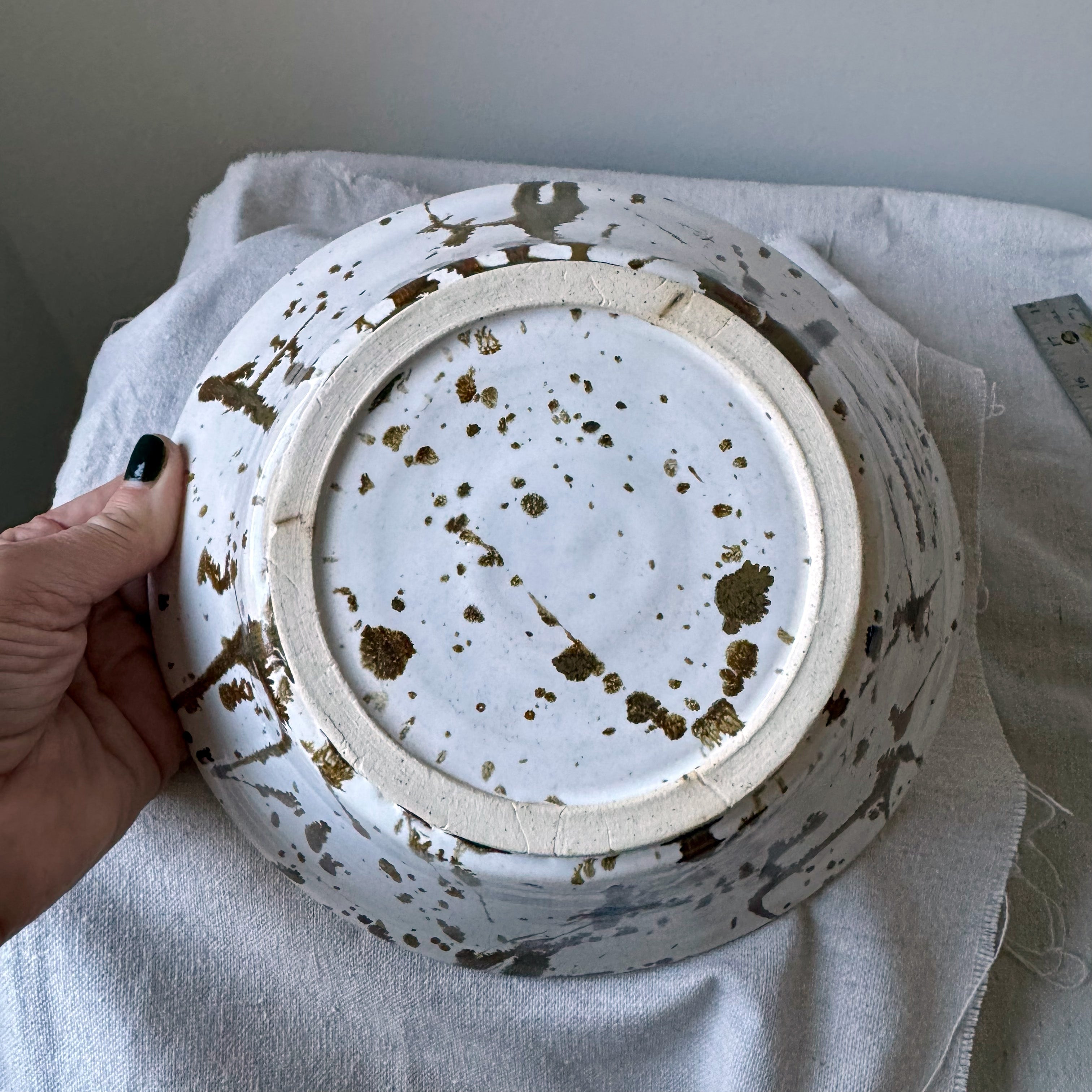 Ceramic bowl with speckled design held by a hand on a white cloth background