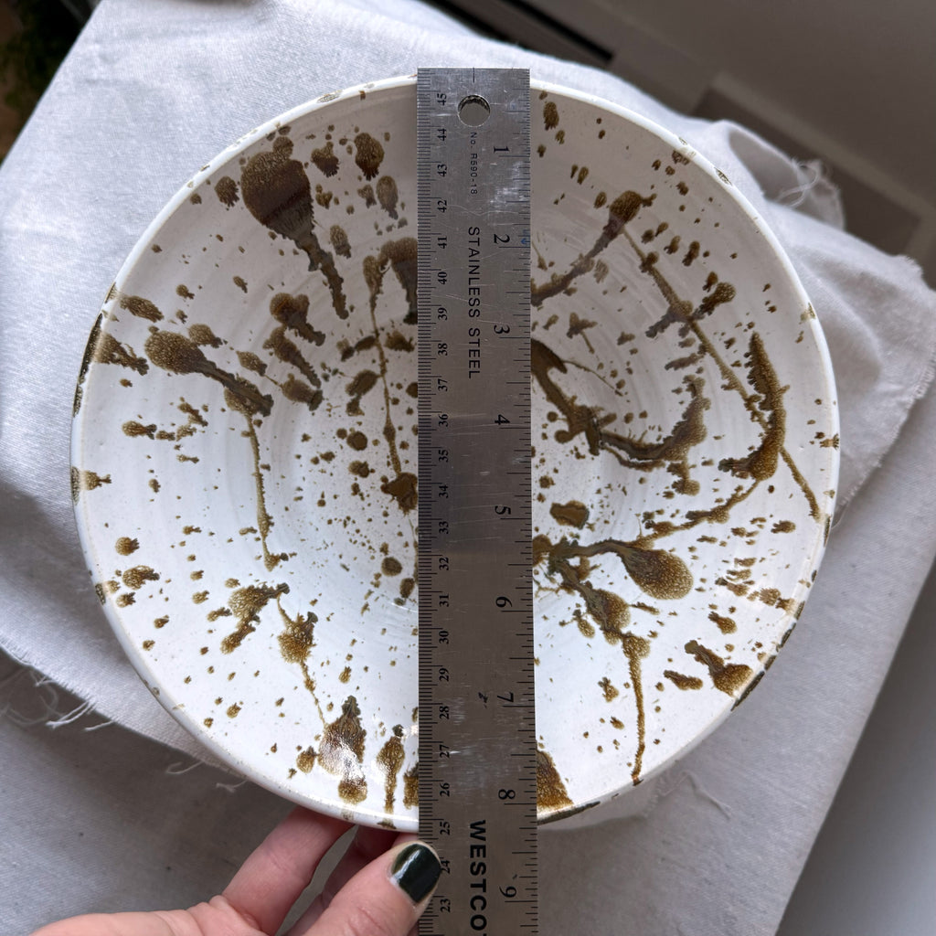 White ceramic plate with brown speckles and a ruler for scale on a white cloth background