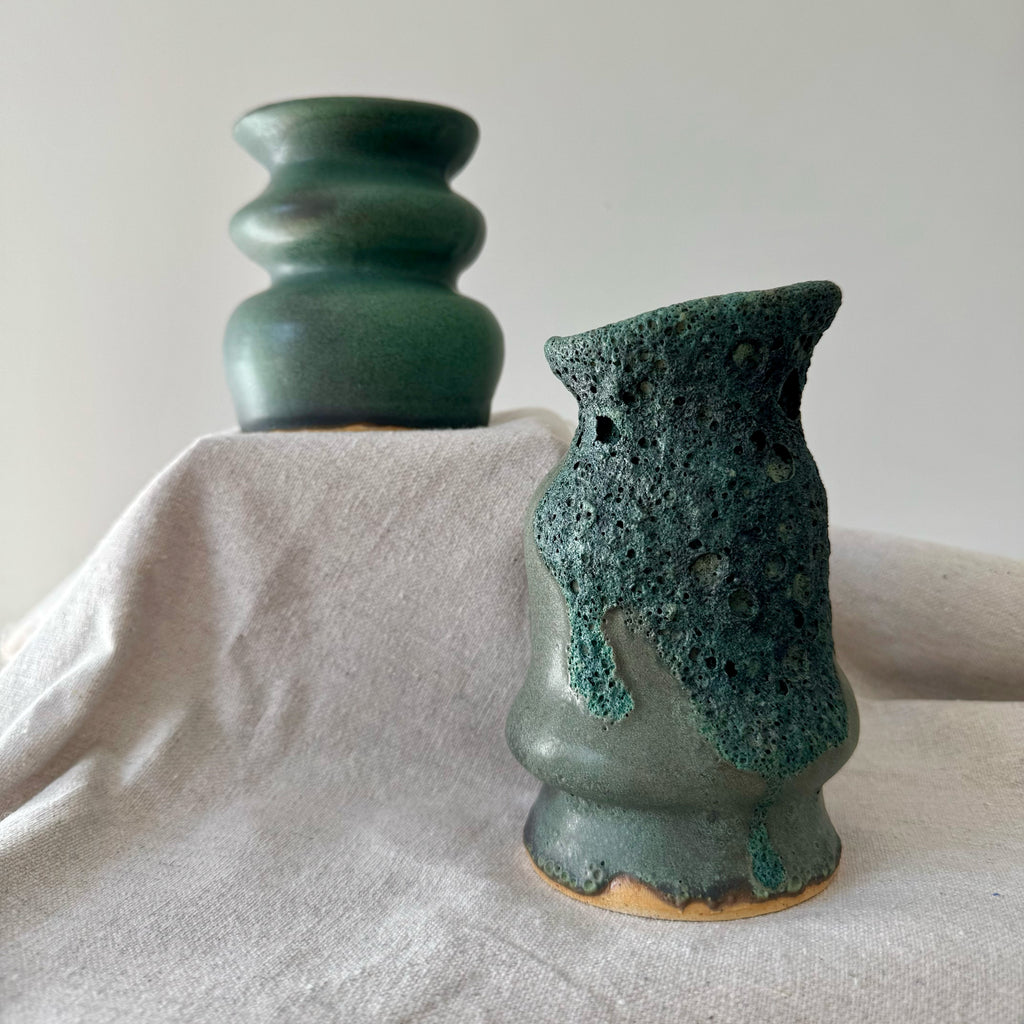Two green ceramic vases on a light fabric surface with a plain background