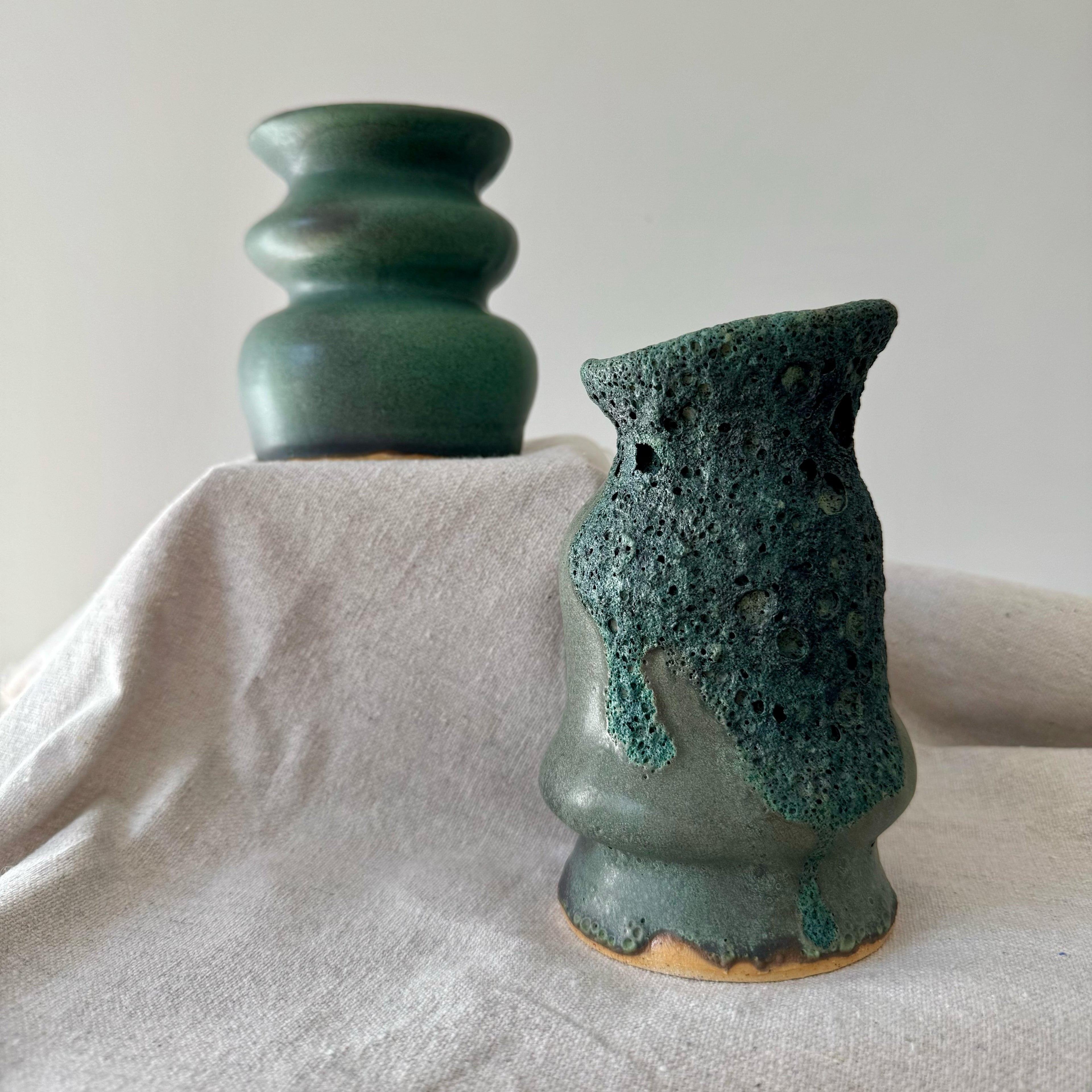 Two green ceramic vases on a light fabric surface with a plain background