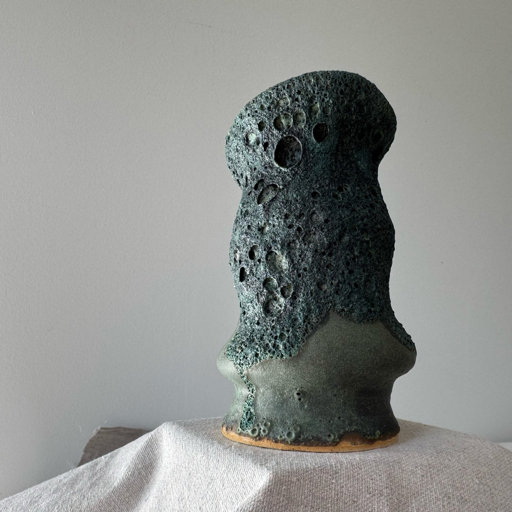Textured green ceramic sculpture on a white surface with a plain background