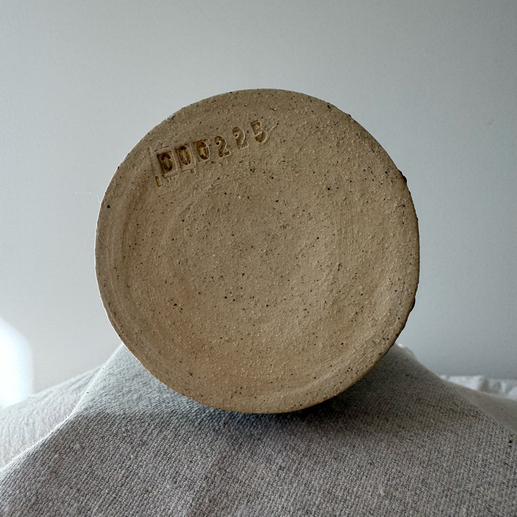 Round brown ceramic object with a visible brand mark on a textured surface.
