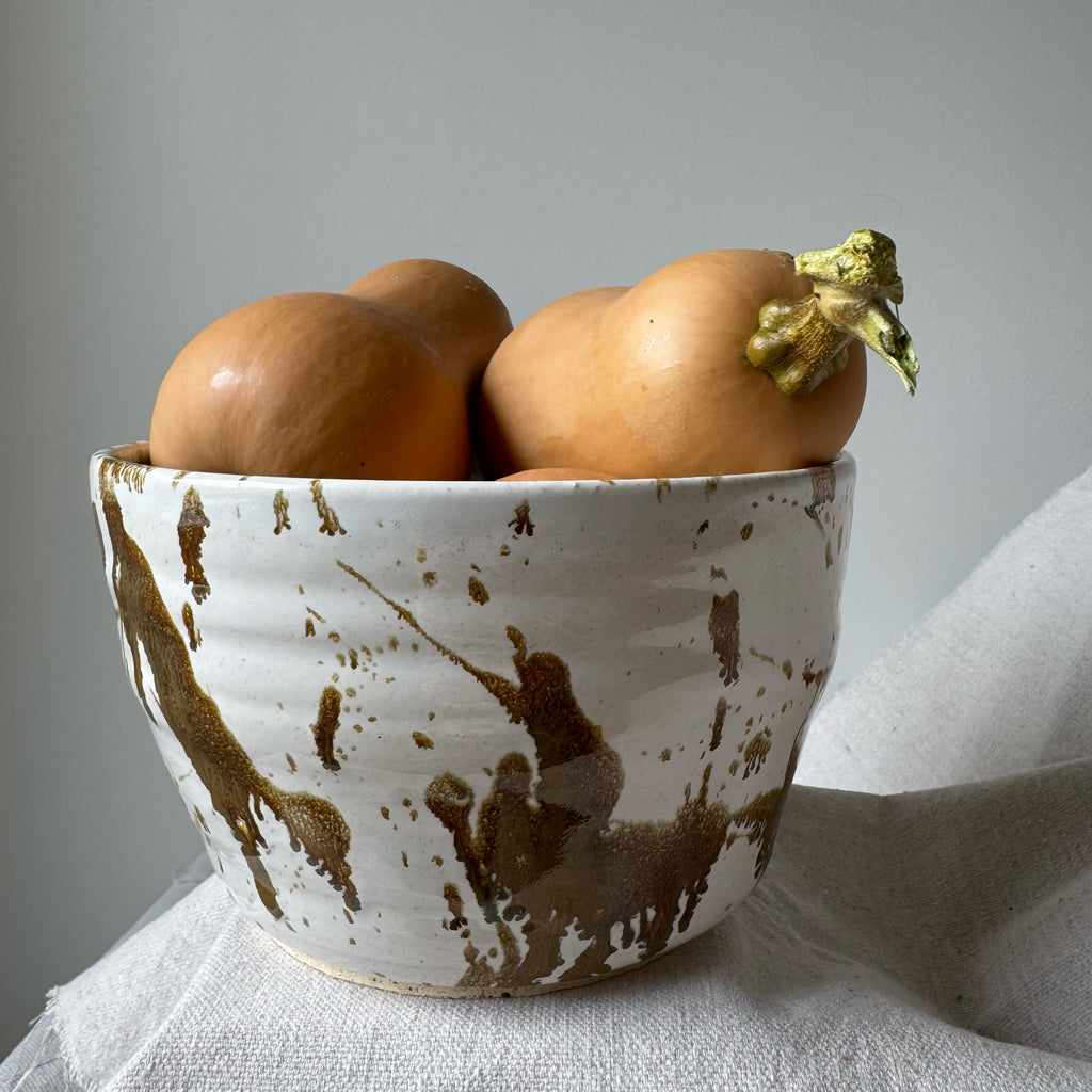 White ceramic bowl with brown speckles containing three potatoes on a light gray background