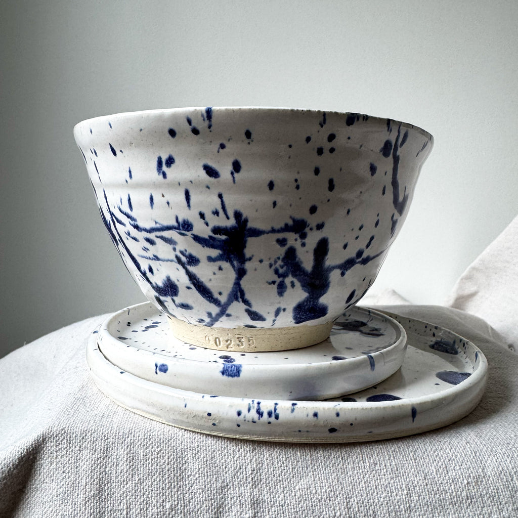 Ceramic bowl with blue splatter design on a matching plate against a neutral background
