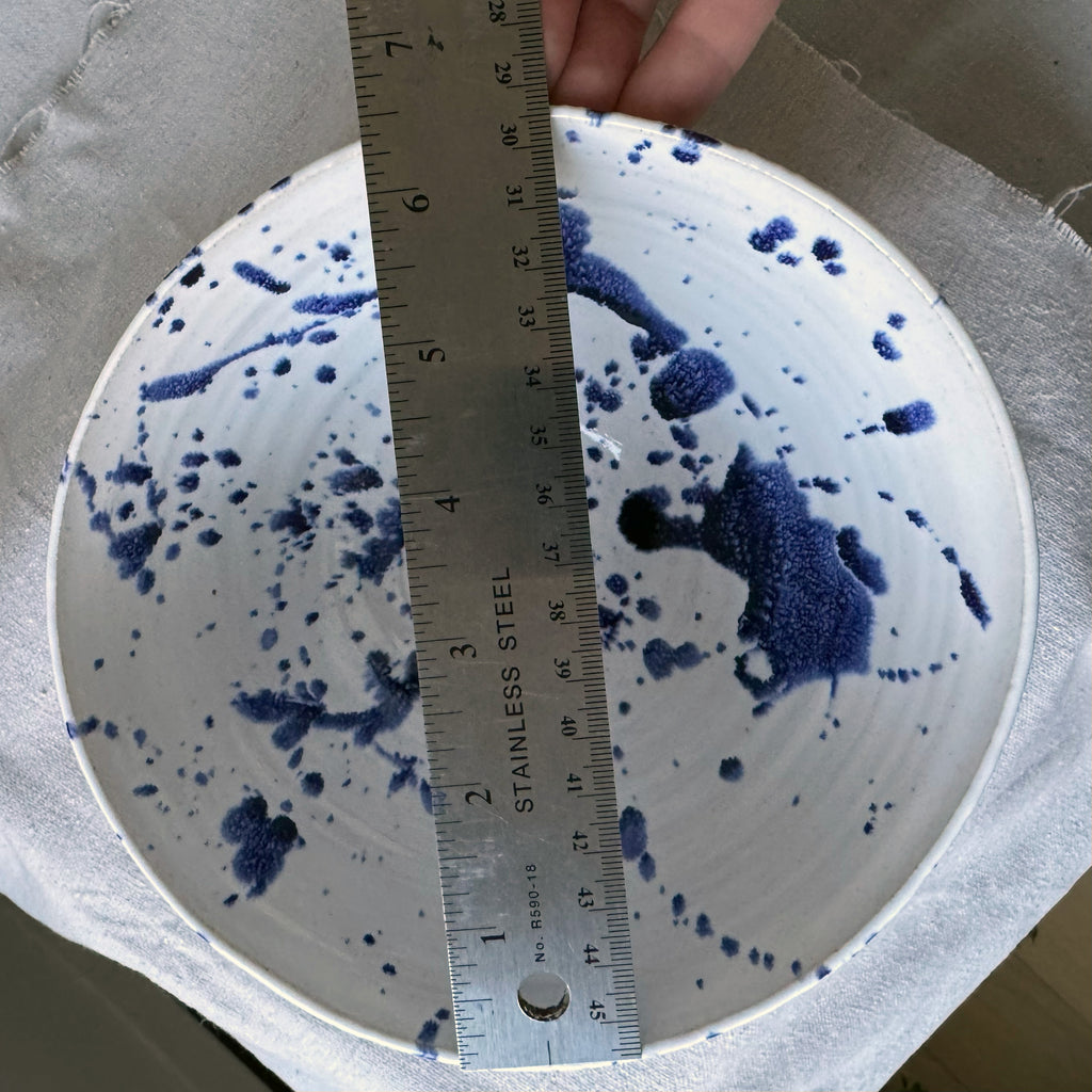 White ceramic bowl with blue splashes and a ruler for scale on a gray surface.
