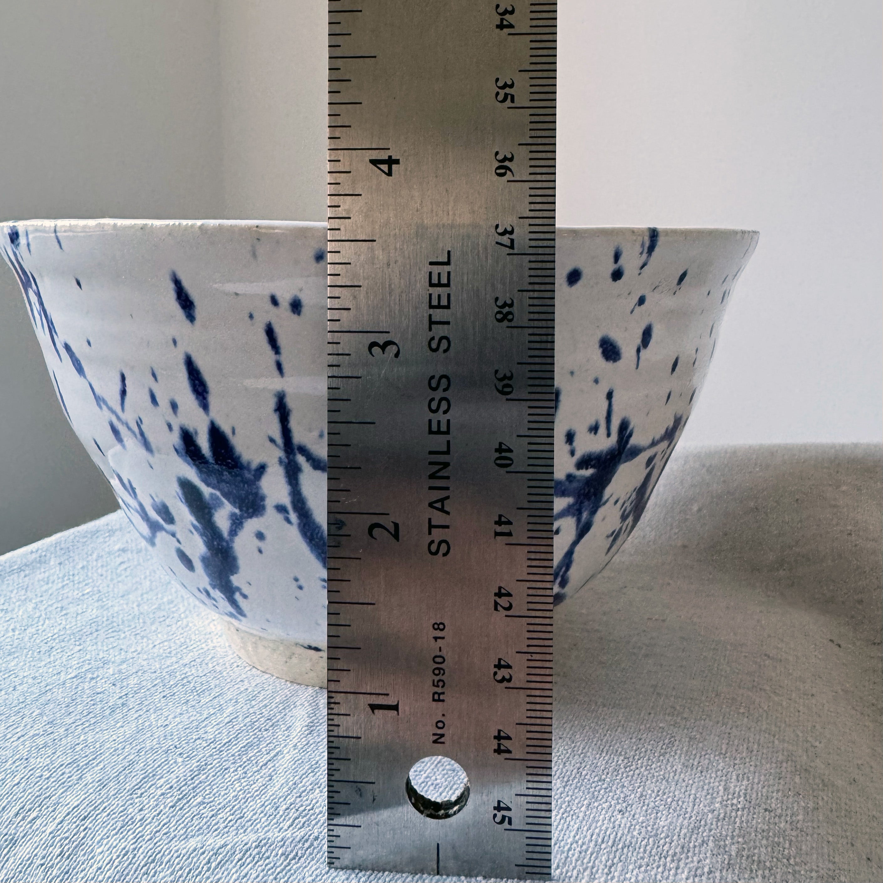 Ceramic bowl with blue splatter design next to a ruler for scale on a light gray surface.