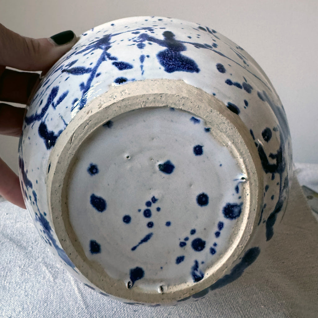 Ceramic vase with blue splatter design held by a hand on a light background