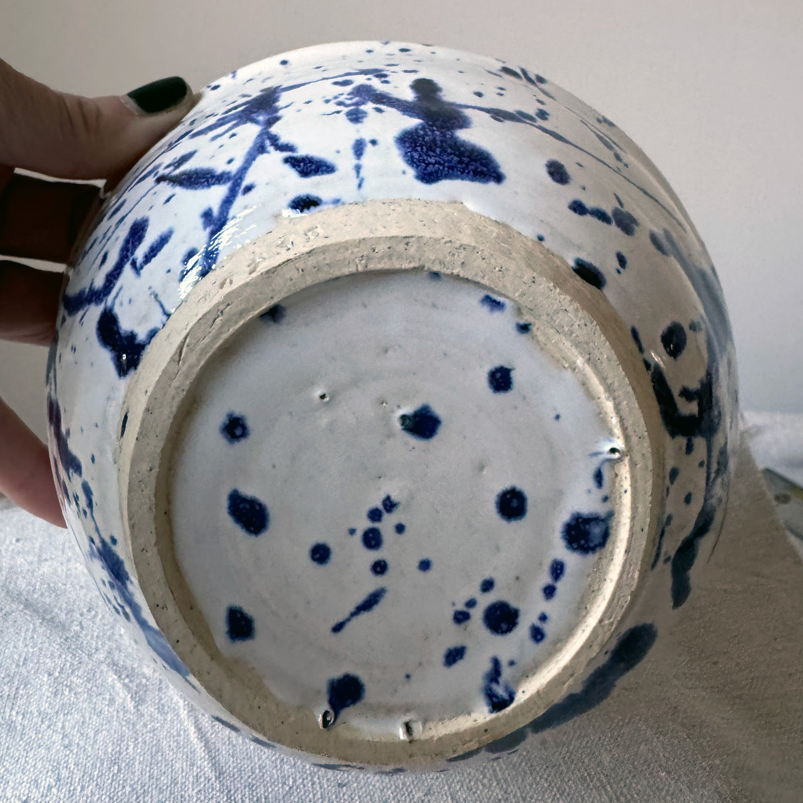 Ceramic vase with blue splatter design held by a hand on a light background