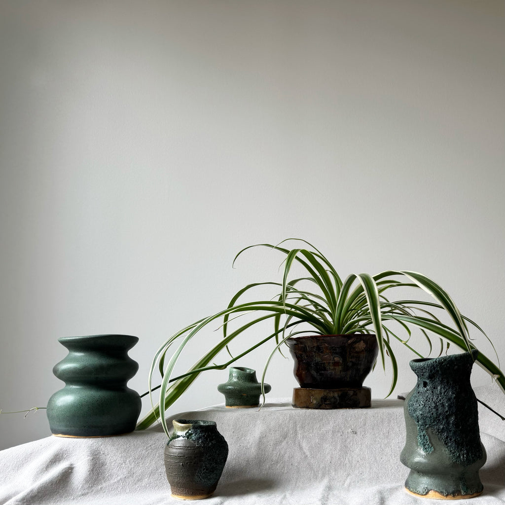 Collection of green ceramic pots and a plant on a light surface with a neutral background