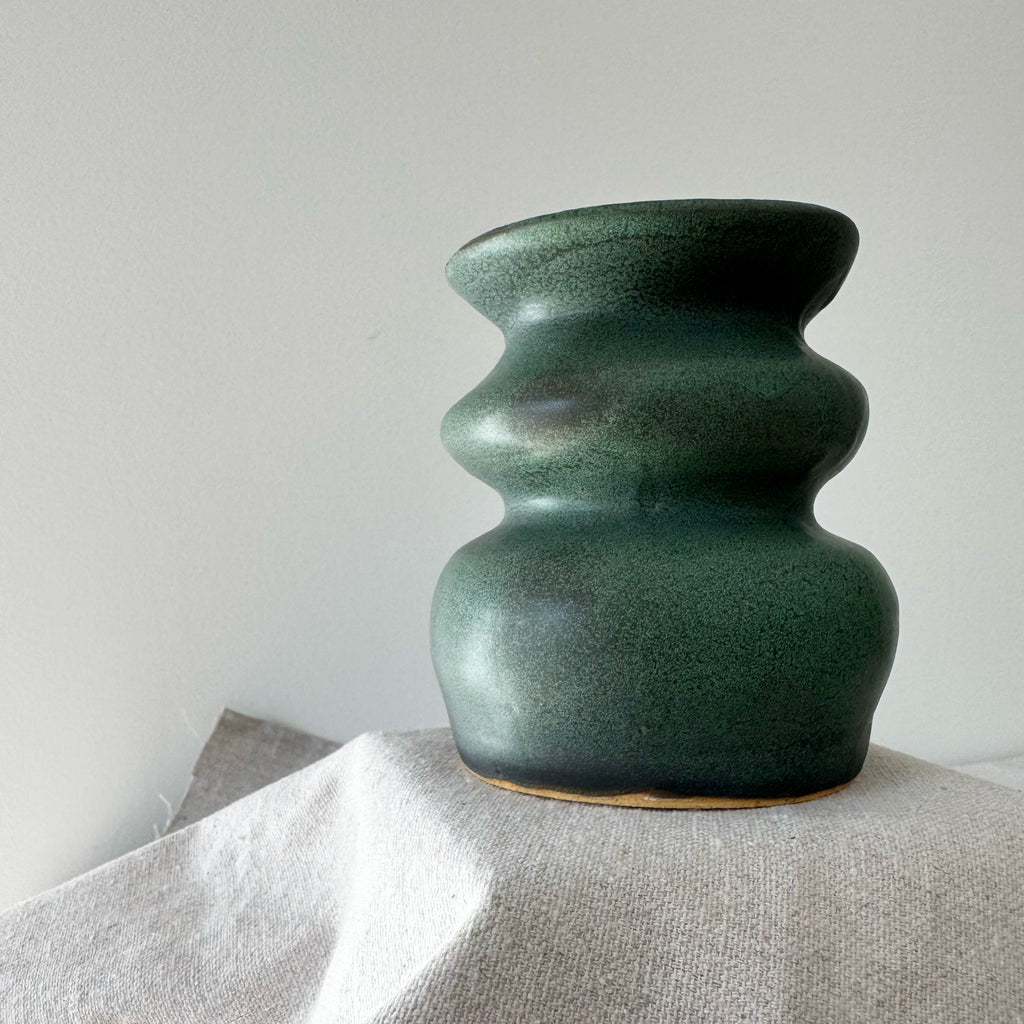 Green ceramic vase on a light fabric surface with a plain background