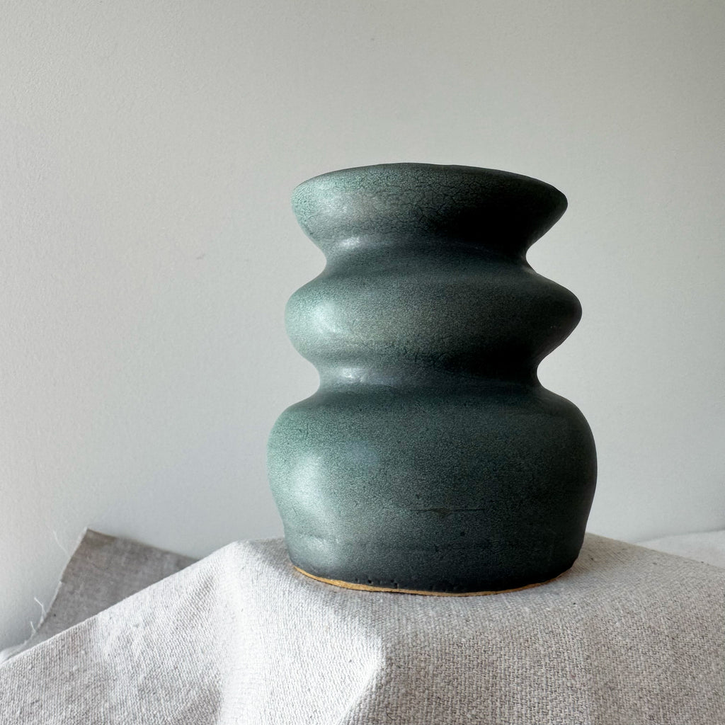 Green ceramic vase on a textured surface with a plain background