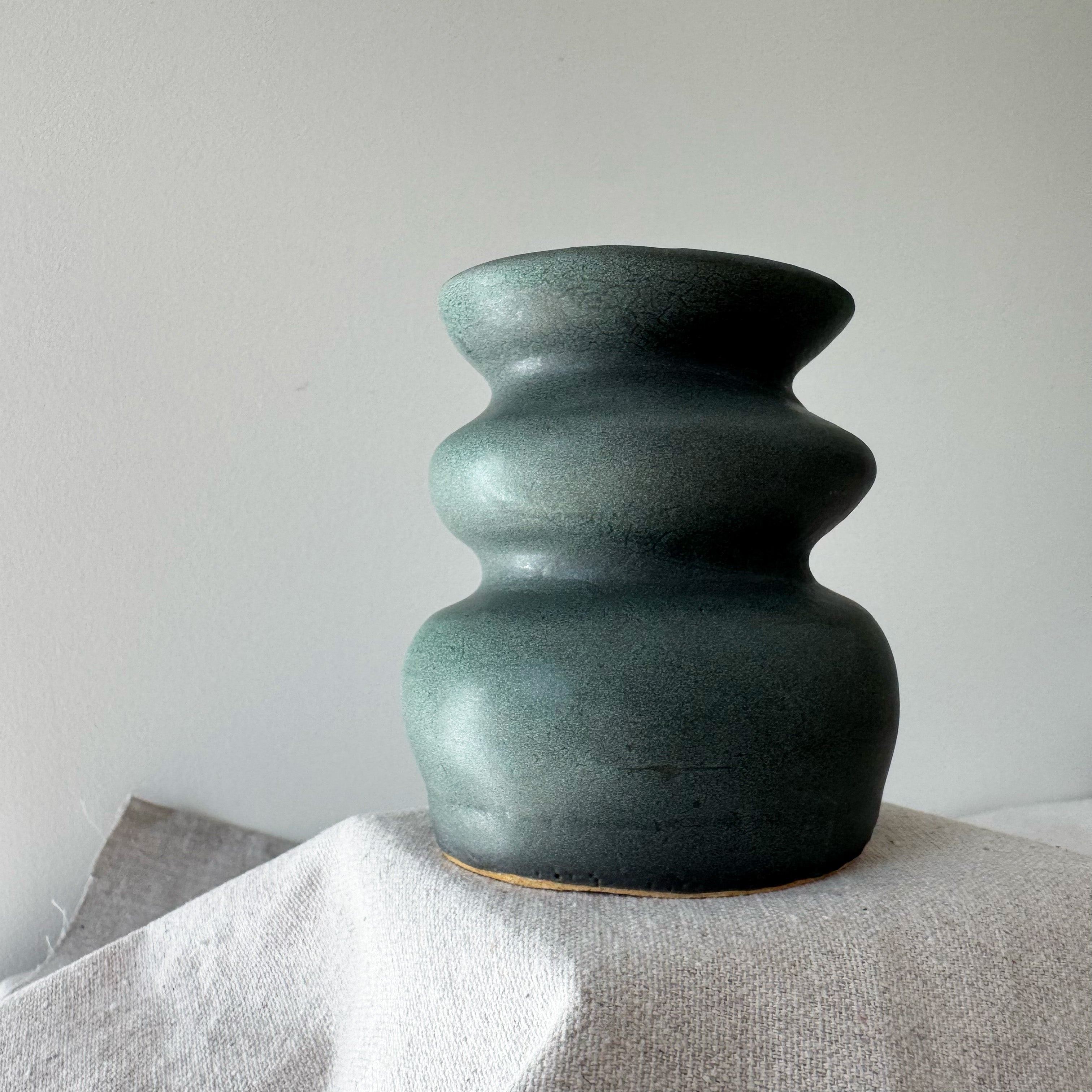 Green ceramic vase on a textured surface with a plain background