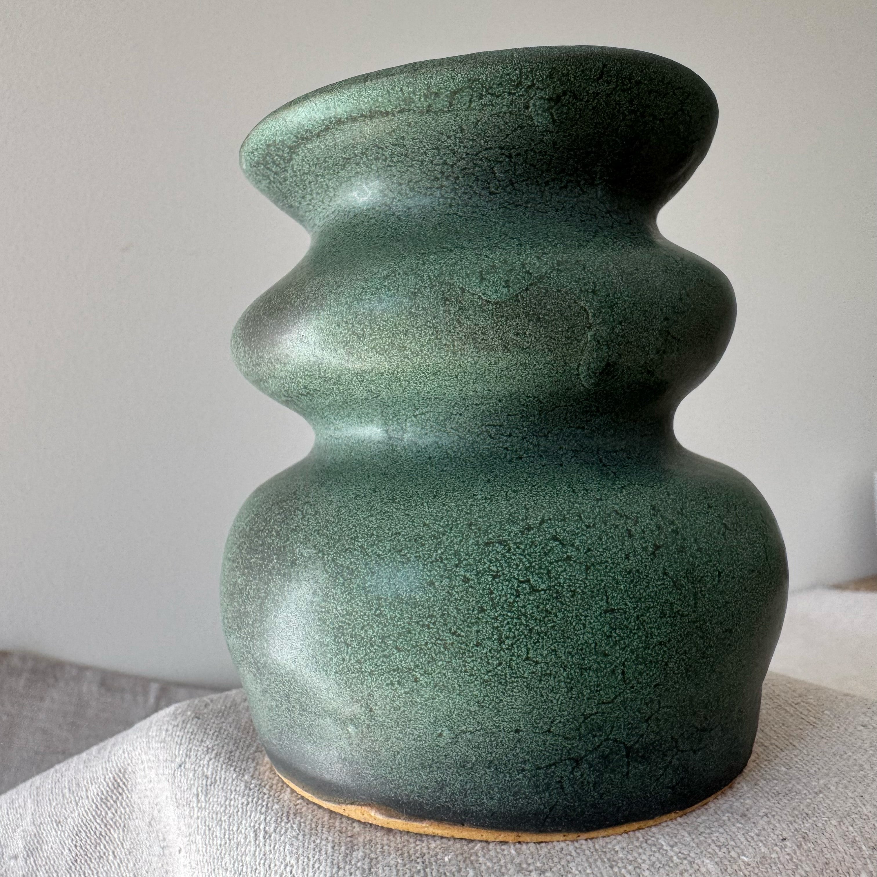 Green ceramic vase with textured surface on a neutral background