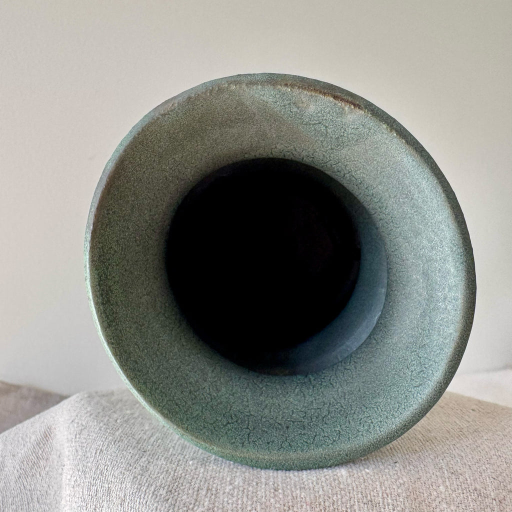 Green ceramic vase on a light gray surface with a neutral background
