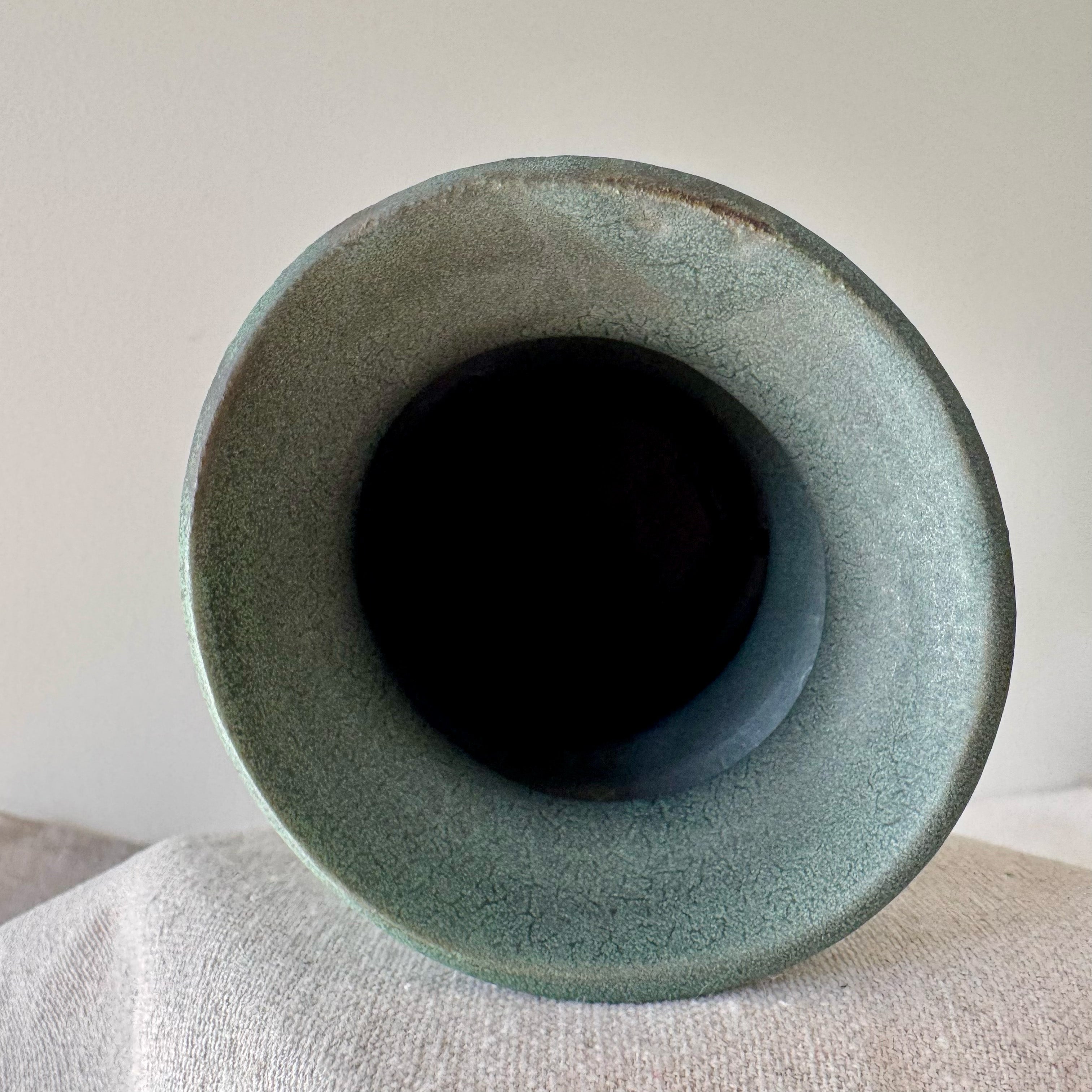 Green ceramic vase on a light gray surface with a neutral background