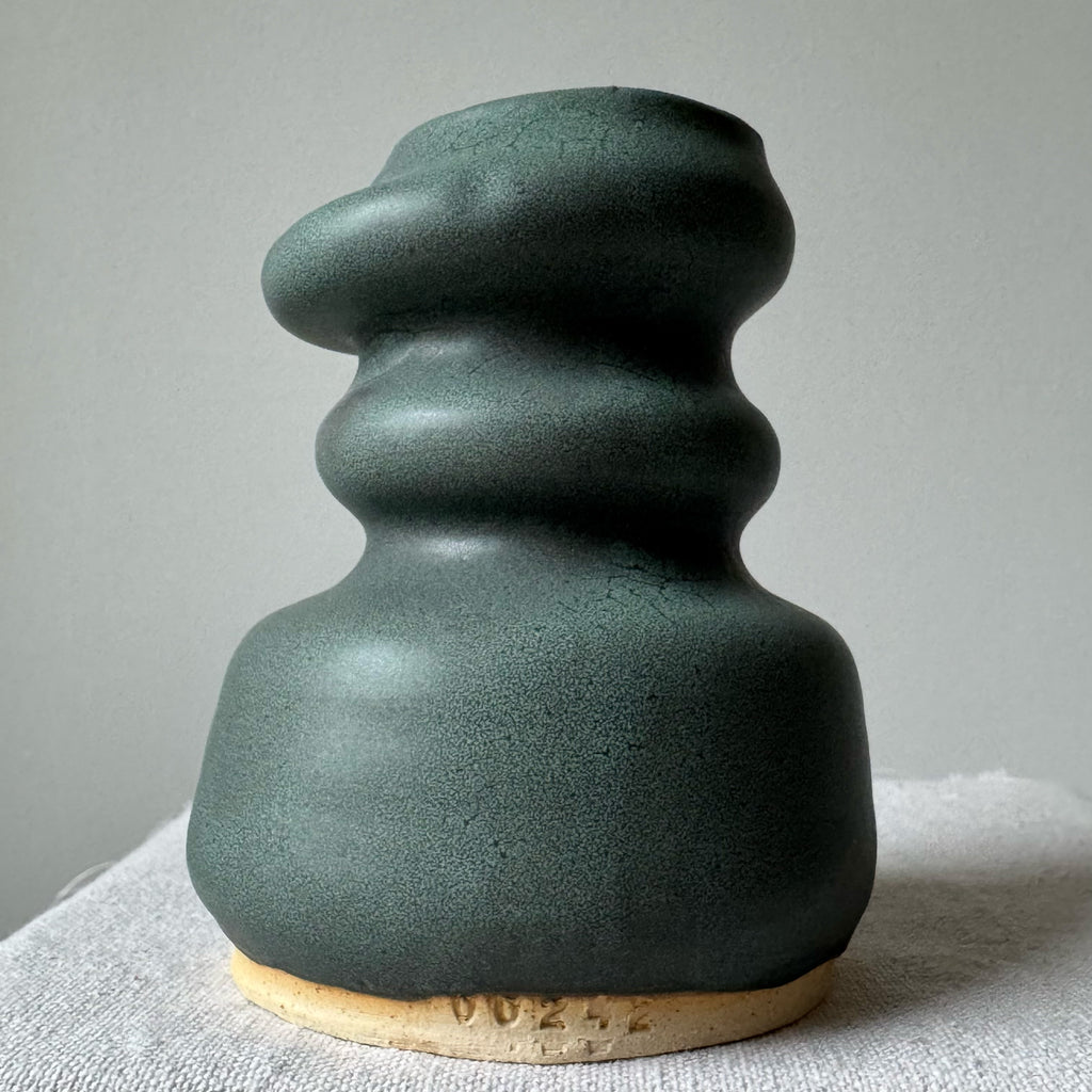 Green ceramic vase with textured surface on a light gray background